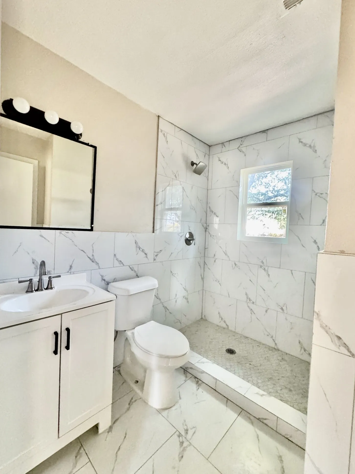 Bathroom featuring a walk-in shower with tile surround, a single vanity with a rectangular sink, and a framed mirror with overhead lighting