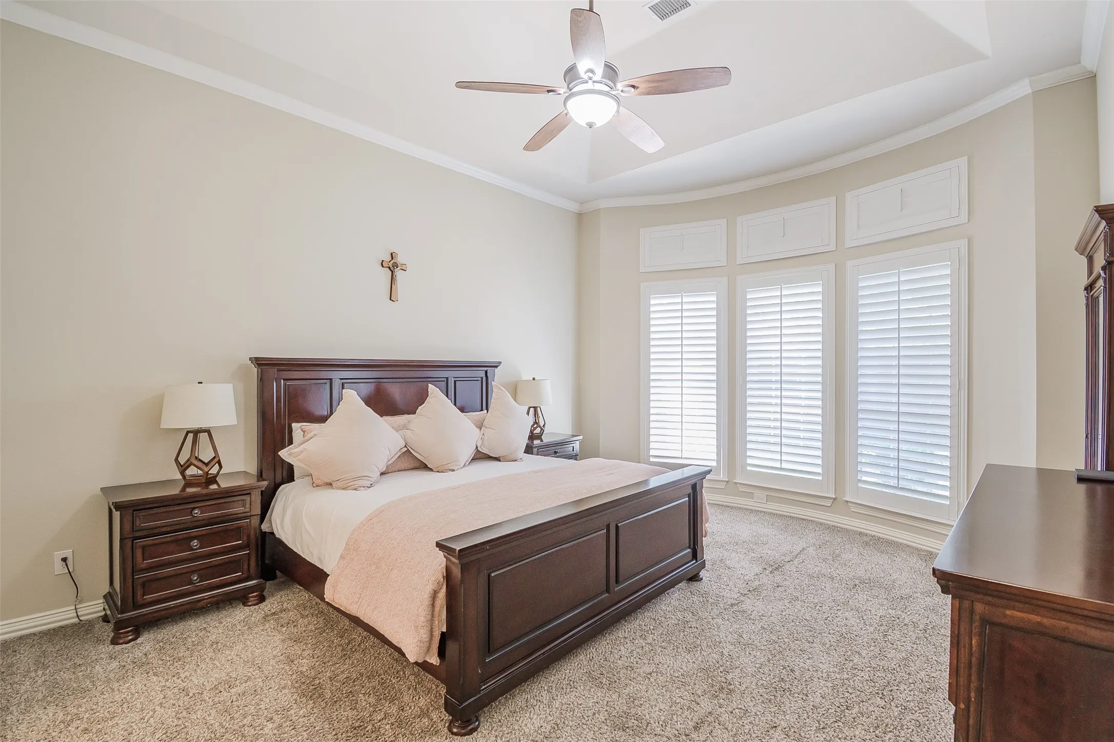 Spacious primary bedroom featuring dark wood architectural detailing, dual nightstands with task lighting, ceiling fan with integrated light fixture, and expansive glass doors with plantation shutters opening to natural light