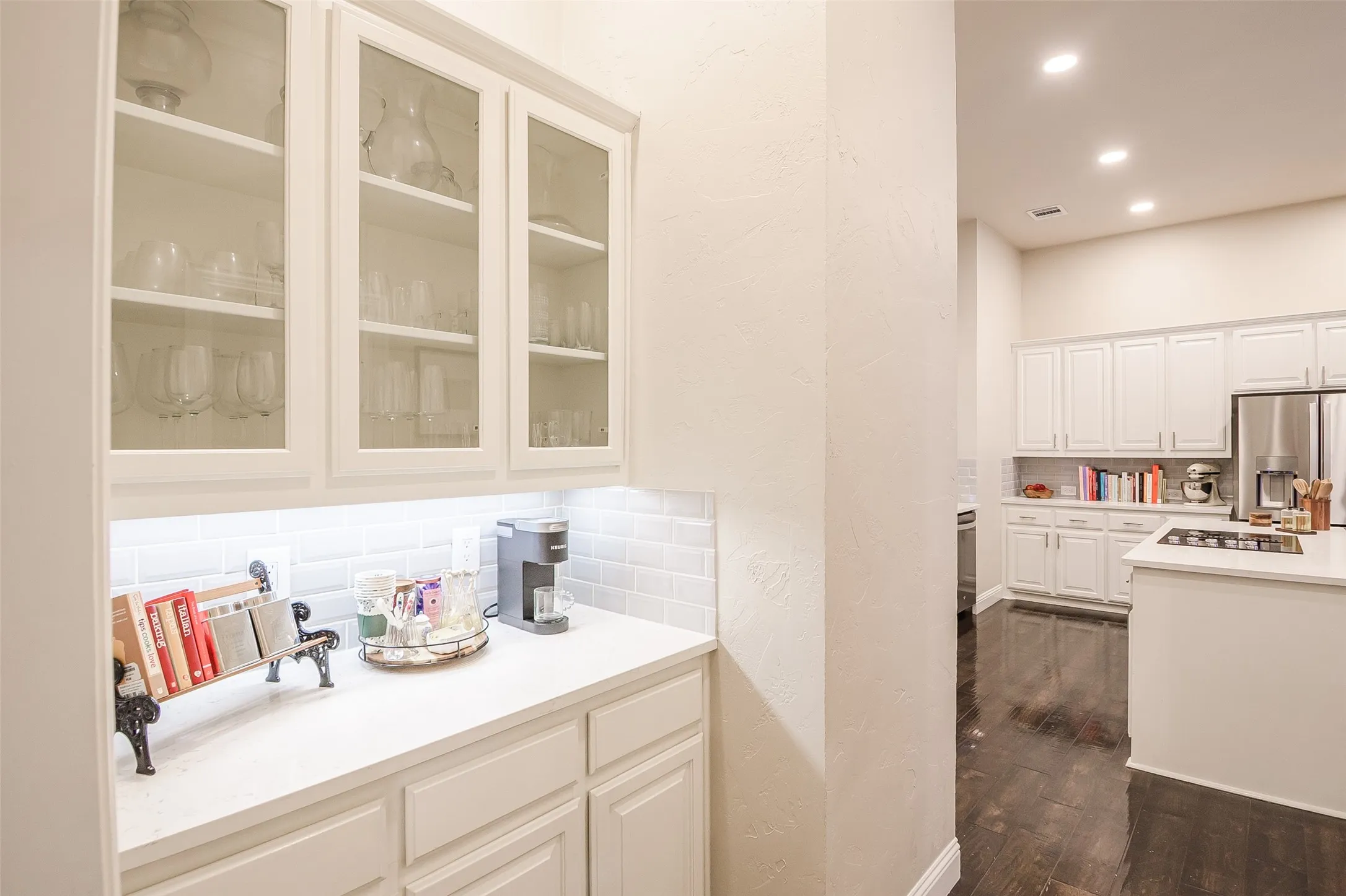 Built-in cabinetry with glass-front uppers, solid surface countertops, subway tile backsplash, and recessed lighting
