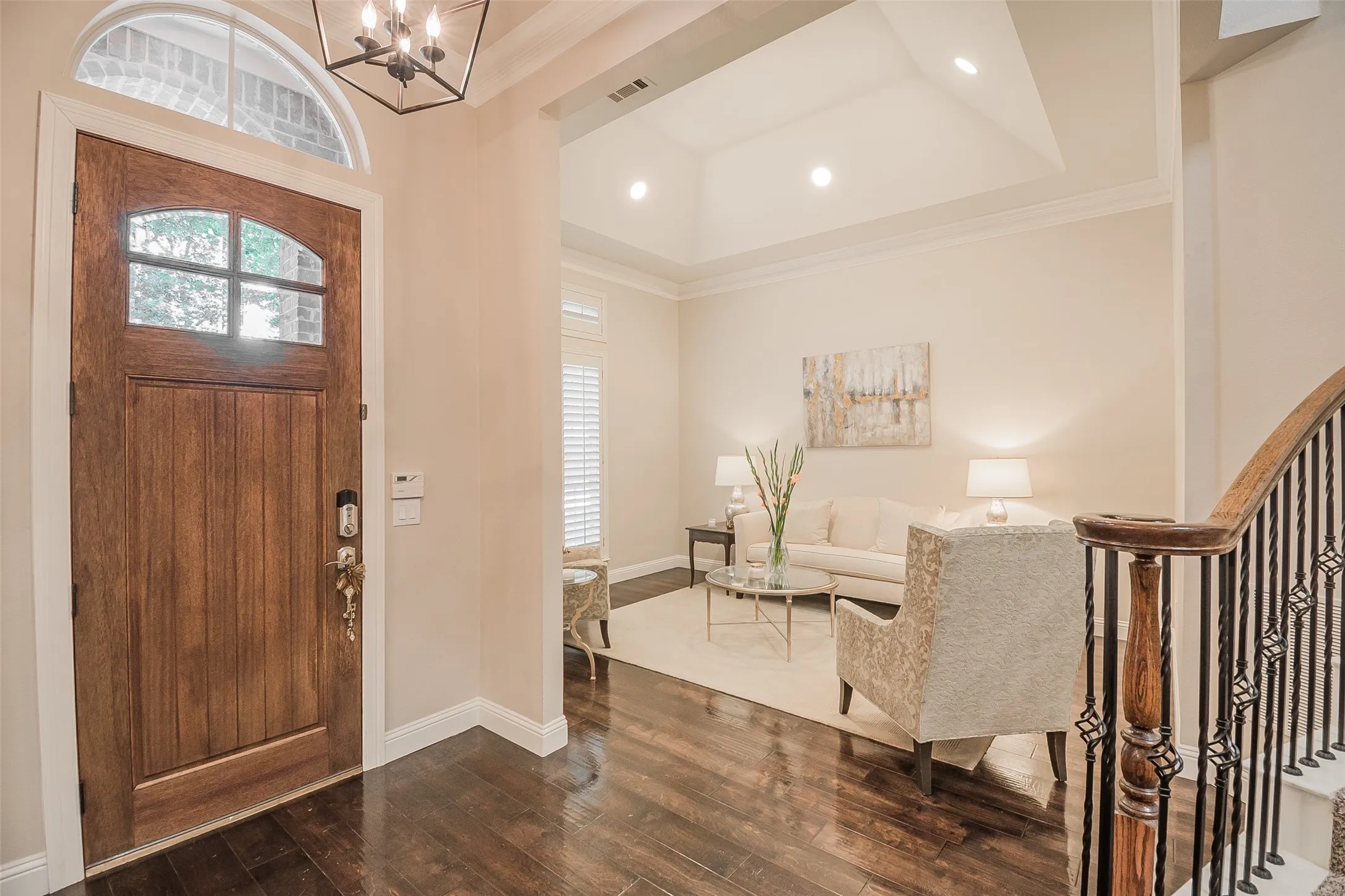 Rich wood-finish flooring, a solid wood entry door with an arched glass panel, and an open-concept living area with a vaulted ceiling
