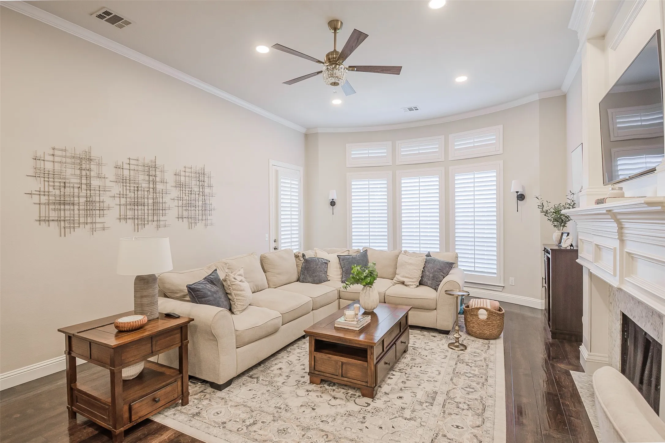Spacious living area featuring dark wood-finish flooring, a decorative fireplace, and large windows with plantation shutters