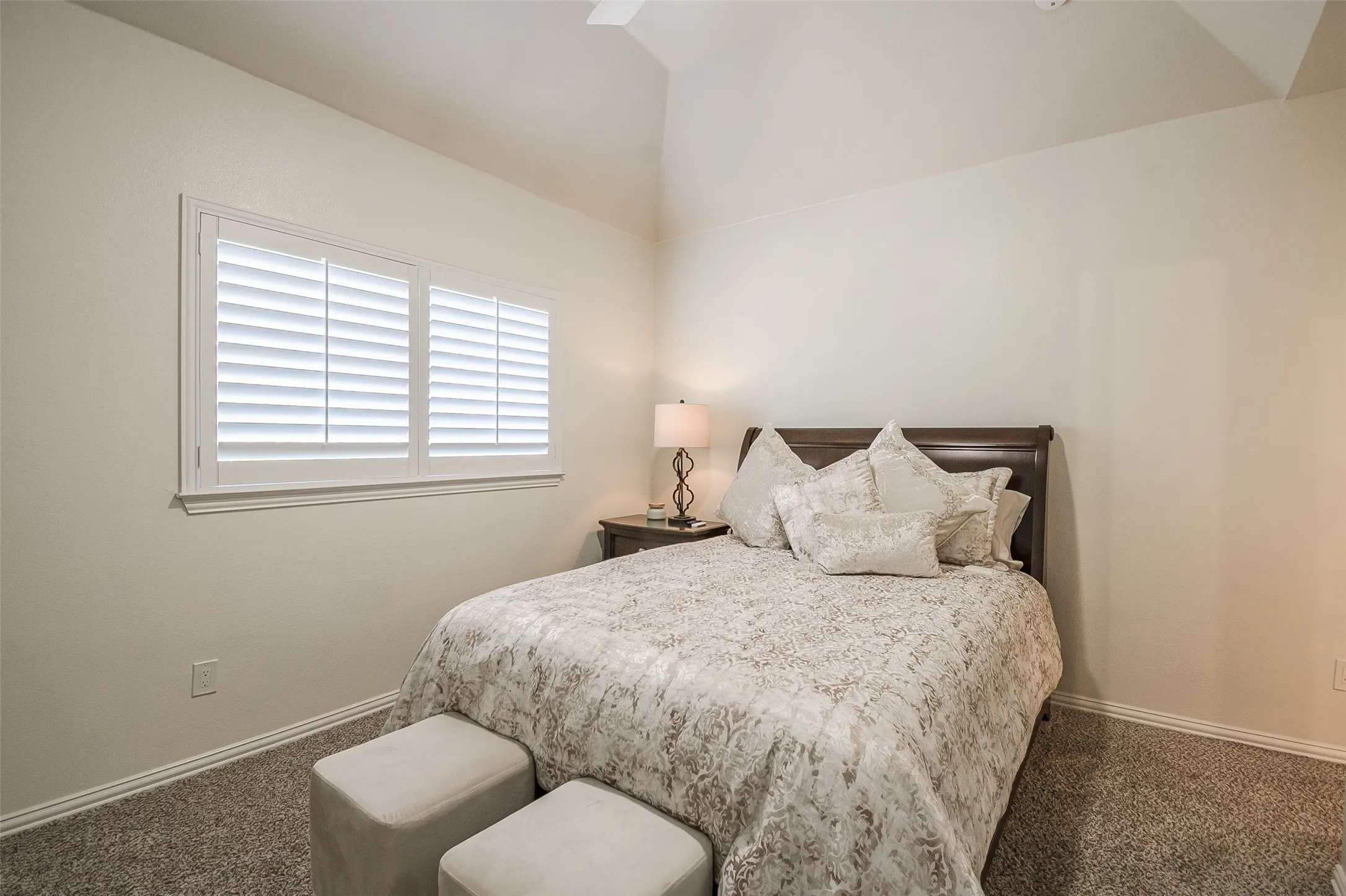 Vaulted ceiling with a ceiling fan, dual windows featuring plantation shutters, and textured wall finish