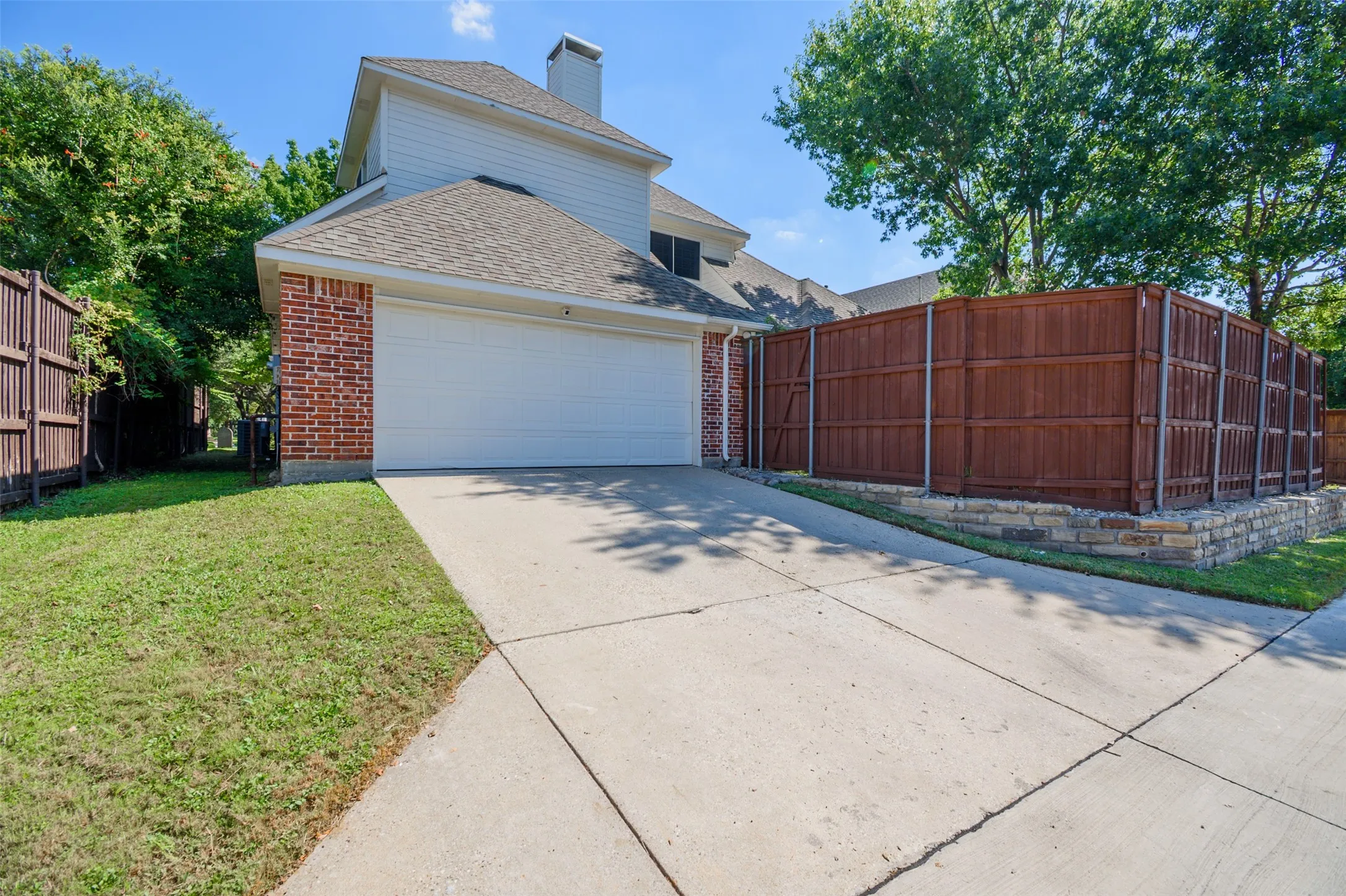 Brick and siding exterior with a two-car garage, concrete driveway, and wood privacy fencing