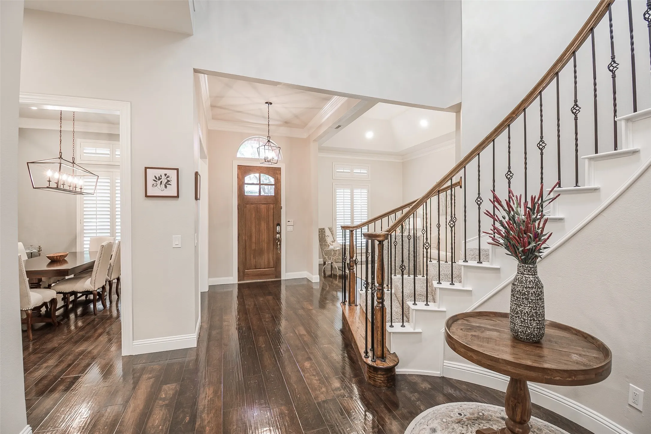 Wood-finish flooring throughout, elegant staircase with wrought iron balusters, arched entryway, and custom wooden front door with glass inserts