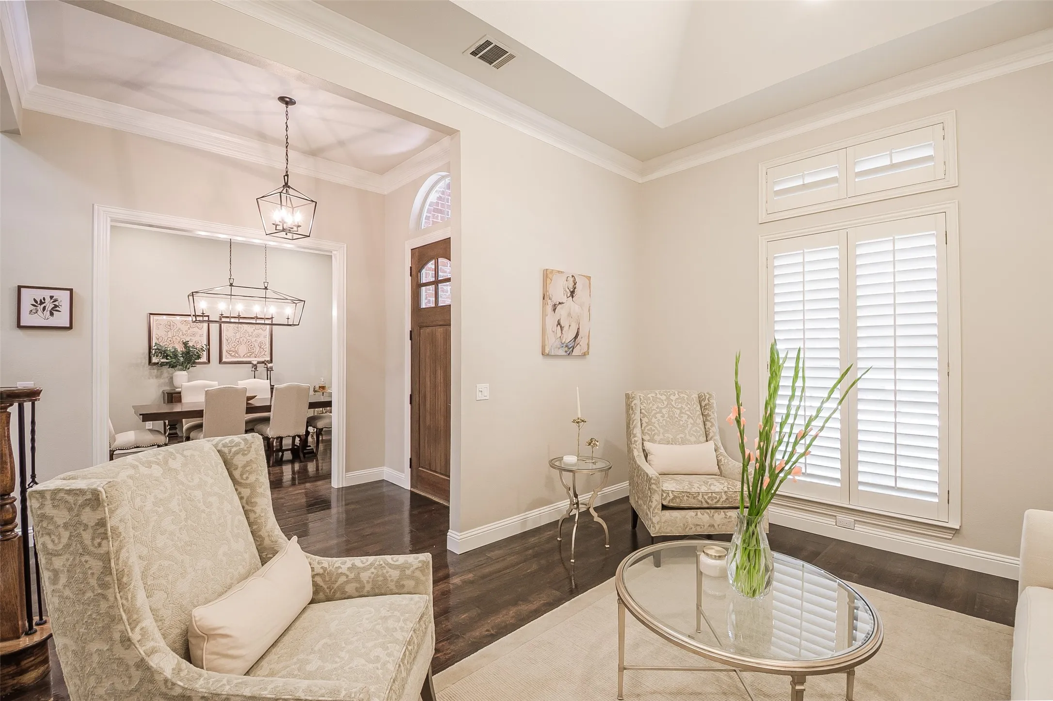 Hardwood flooring throughout, tray ceiling, crown molding, plantation shutters, and a wood entry door with an arched transom
