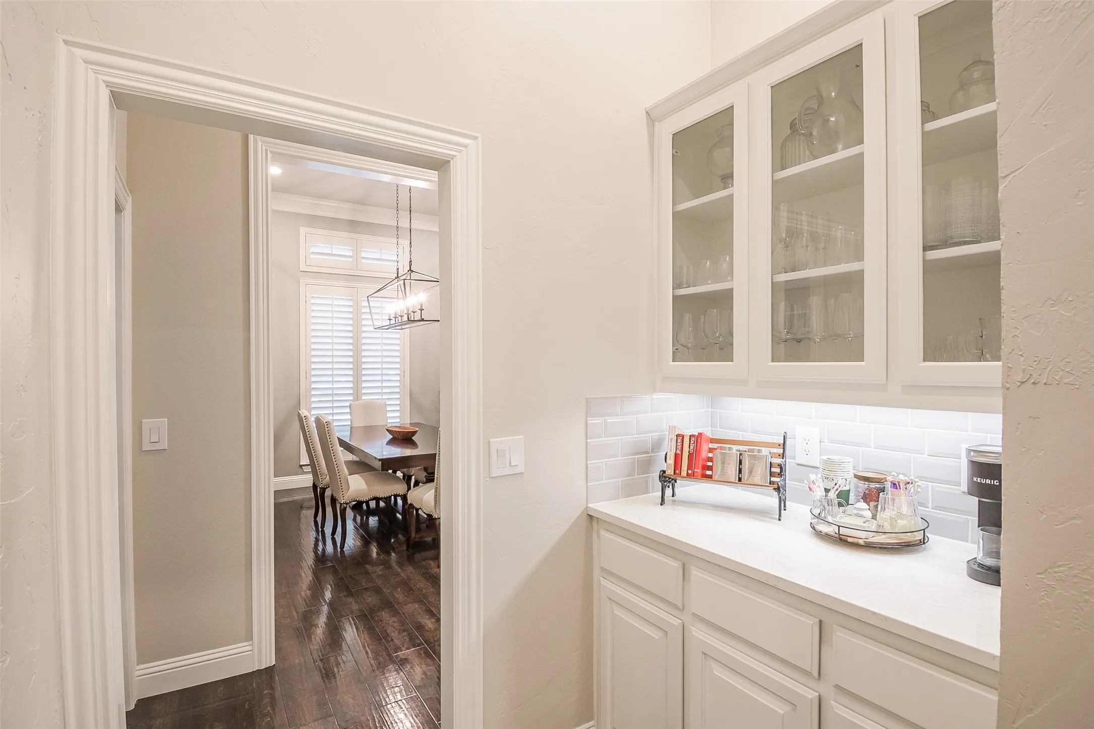 Built-in cabinetry with glass-front uppers, white countertop, white subway tile backsplash, and dark wood-finish flooring