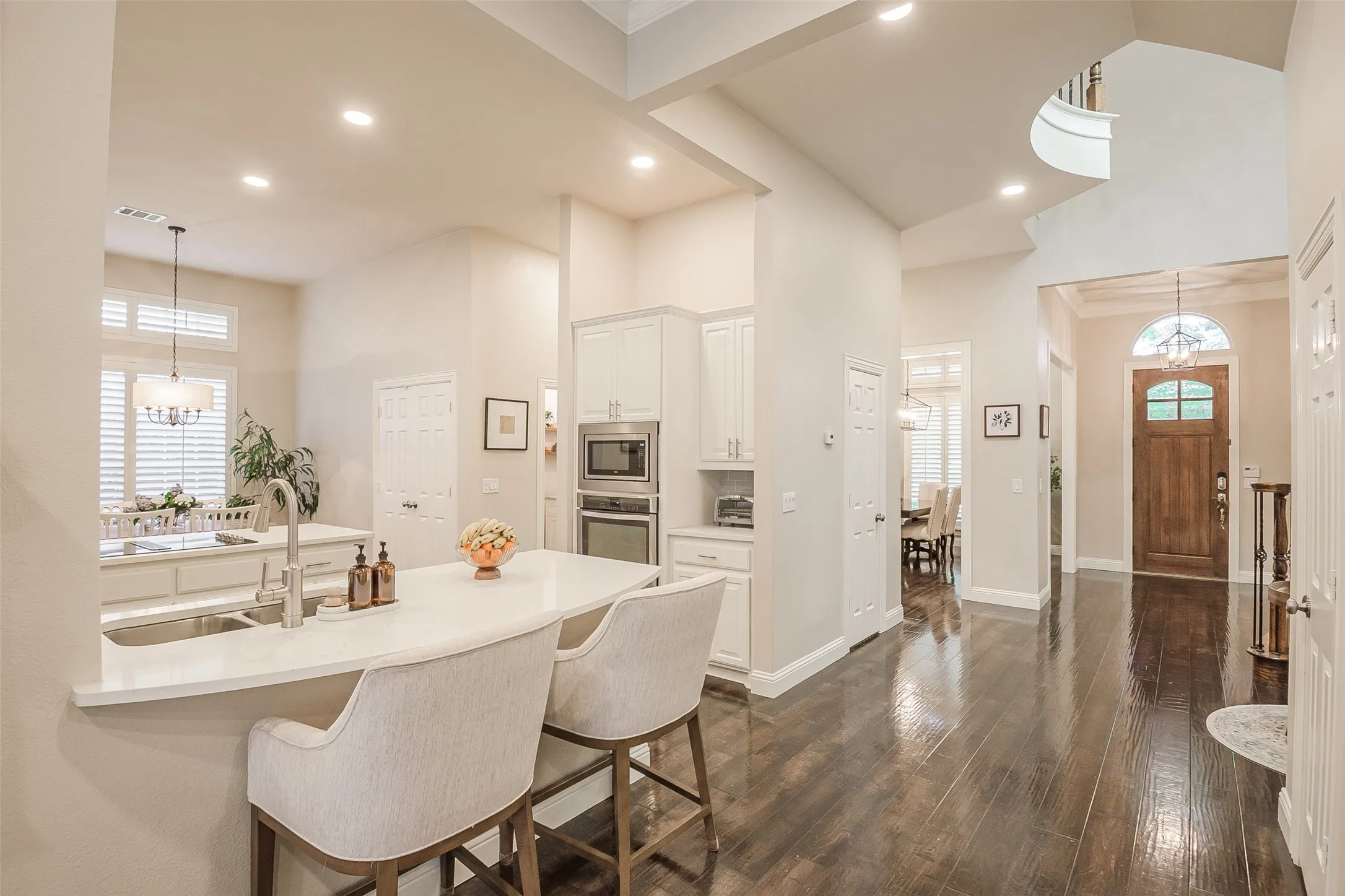 Hardwood-style flooring, a spacious kitchen island with seating, white shaker cabinetry, stainless steel built-in appliances, and a wood-panel entry door with an arched transom