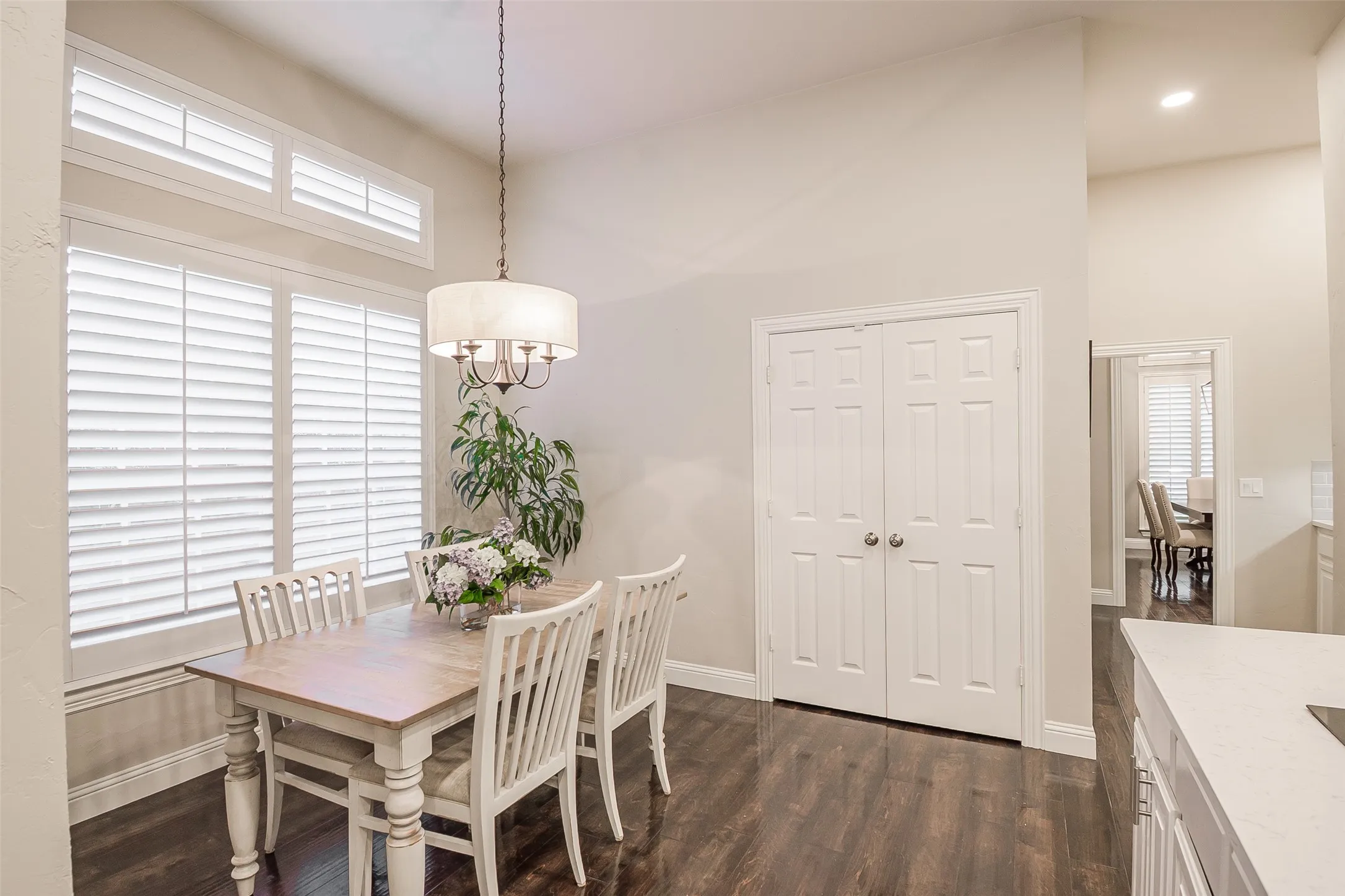 Vaulted ceiling, wood-finish flooring, white plantation shutters, drum pendant light fixture, and two-panel bifold doors