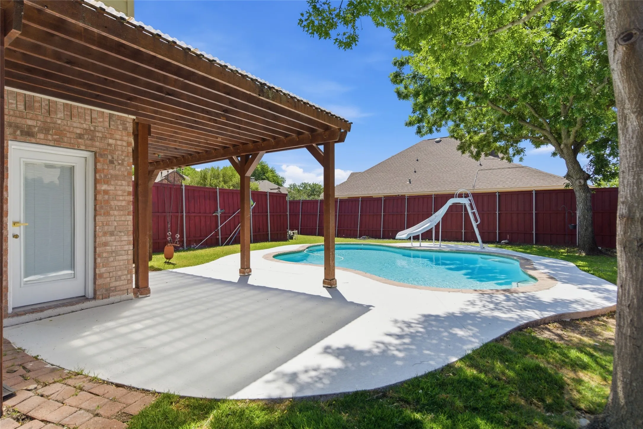 Brick exterior with a covered patio, freeform swimming pool, and a private perimeter fence