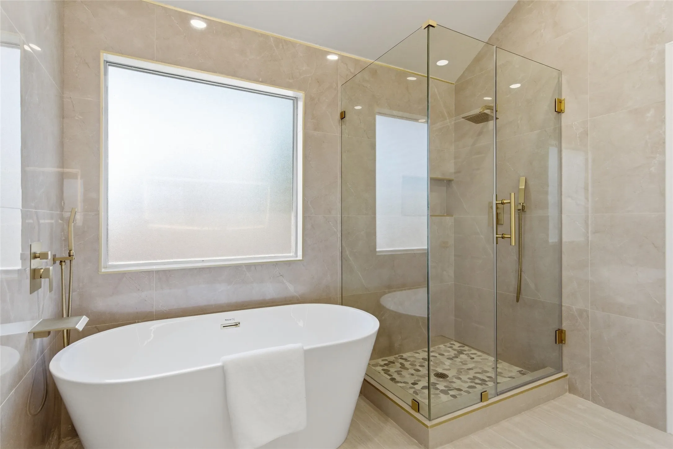 Freestanding soaking tub with brushed brass fixtures, glass-enclosed shower with a mosaic tile floor, and large format wall tiling