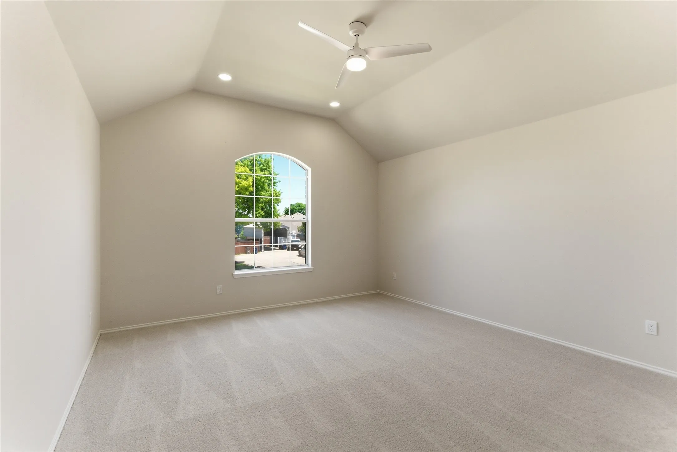 Arched window, vaulted ceiling, flush-mount lighting, ceiling fan, and neutral carpet flooring