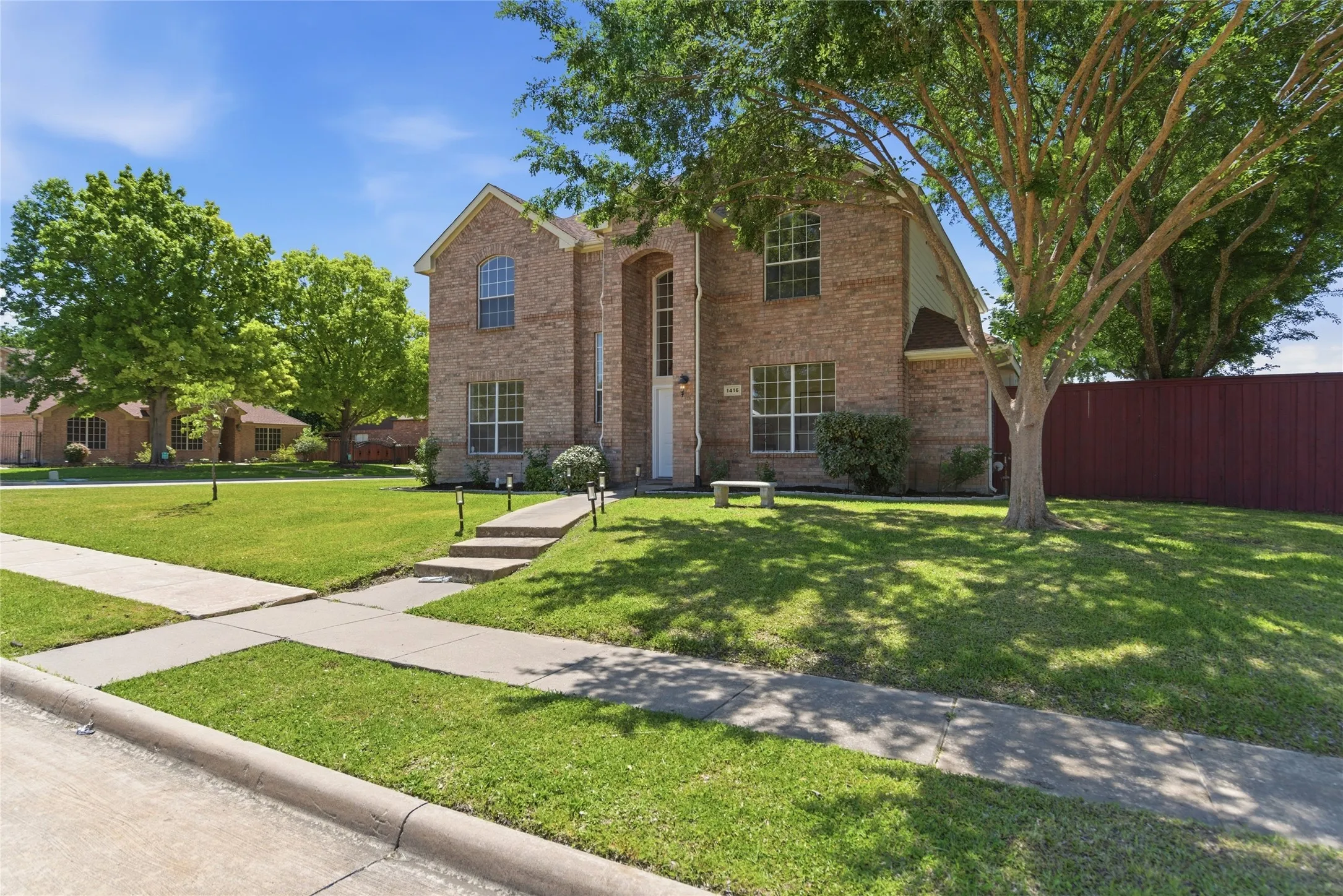 Brick exterior with arched windows, manicured lawn, established trees, and concrete walkways