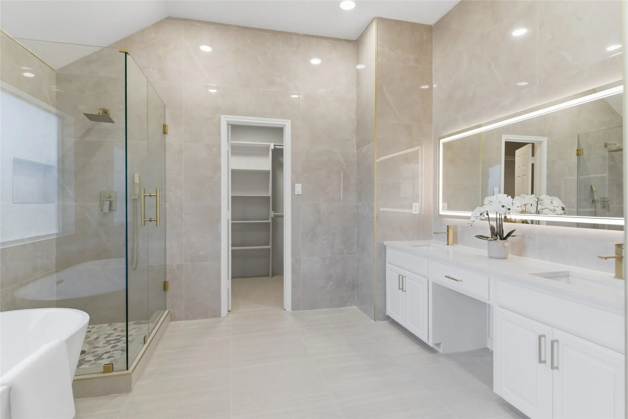 Dual vanity with white cabinetry, gold-finish fixtures, and an integrated illuminated mirror