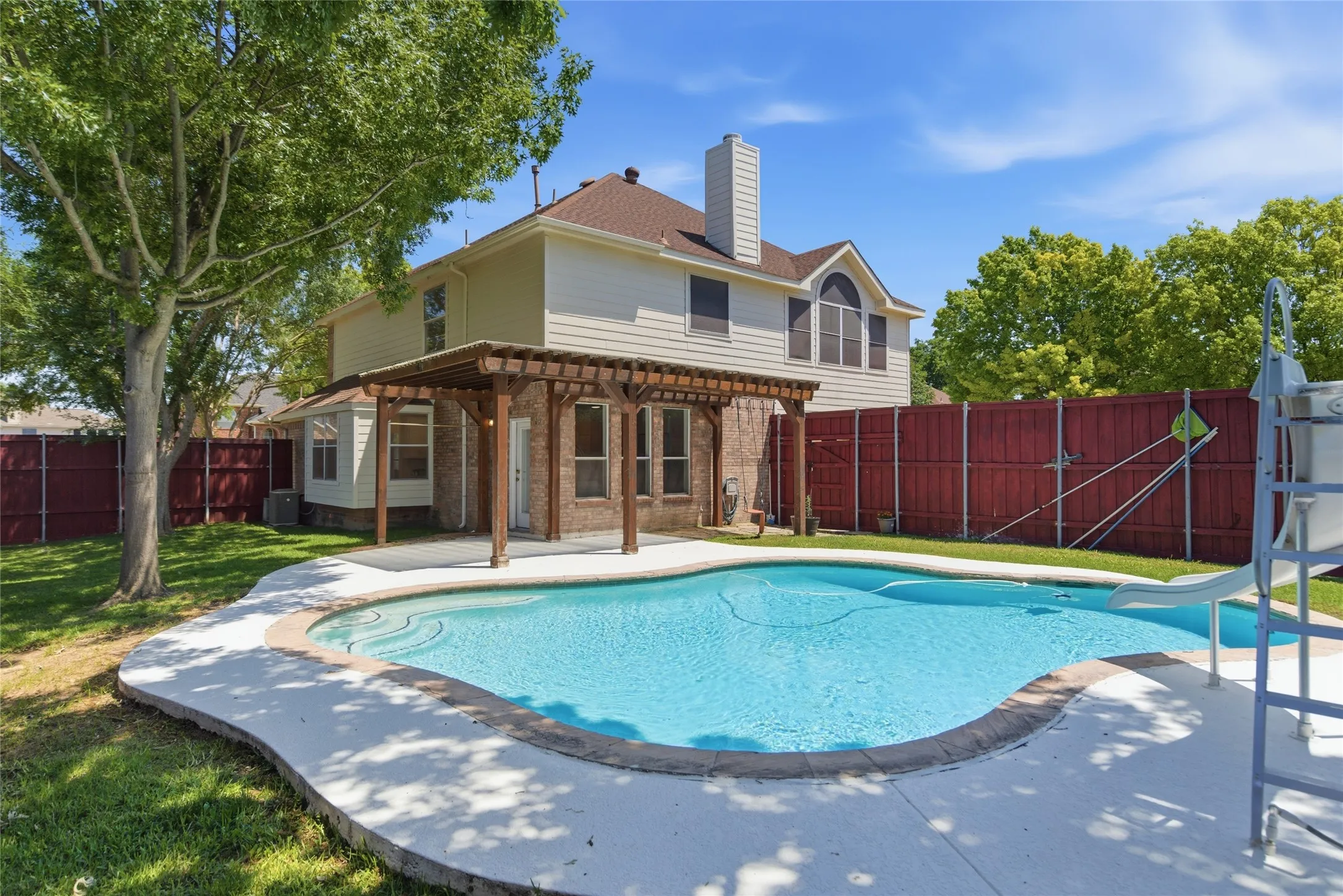 Rear exterior featuring a swimming pool, concrete decking, and a wood pergola