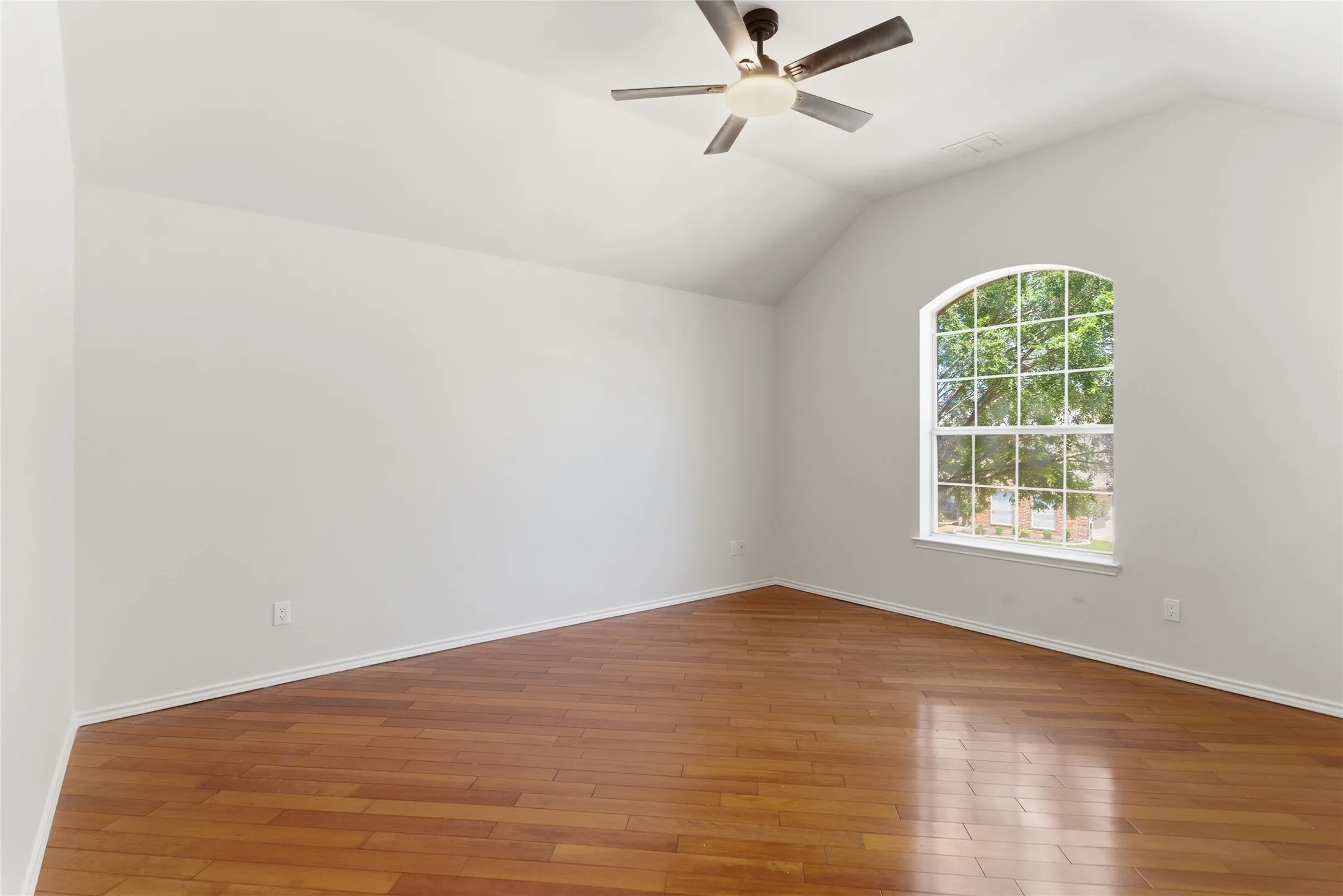 Vaulted ceiling with a ceiling fan light fixture, wood-finish flooring, and an arched window