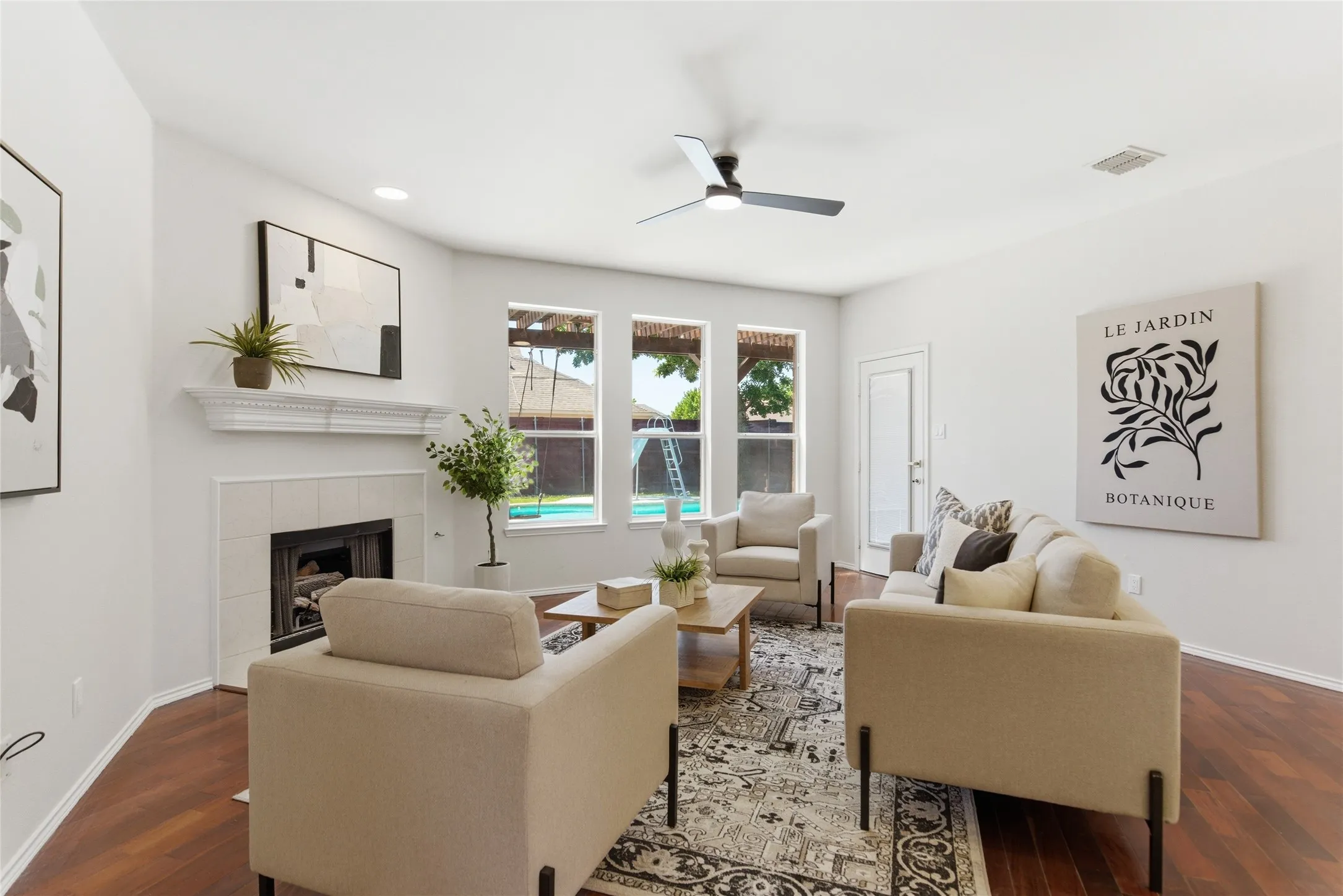 Fireplace with a mantel, three windows, a ceiling fan, and wood-finish flooring