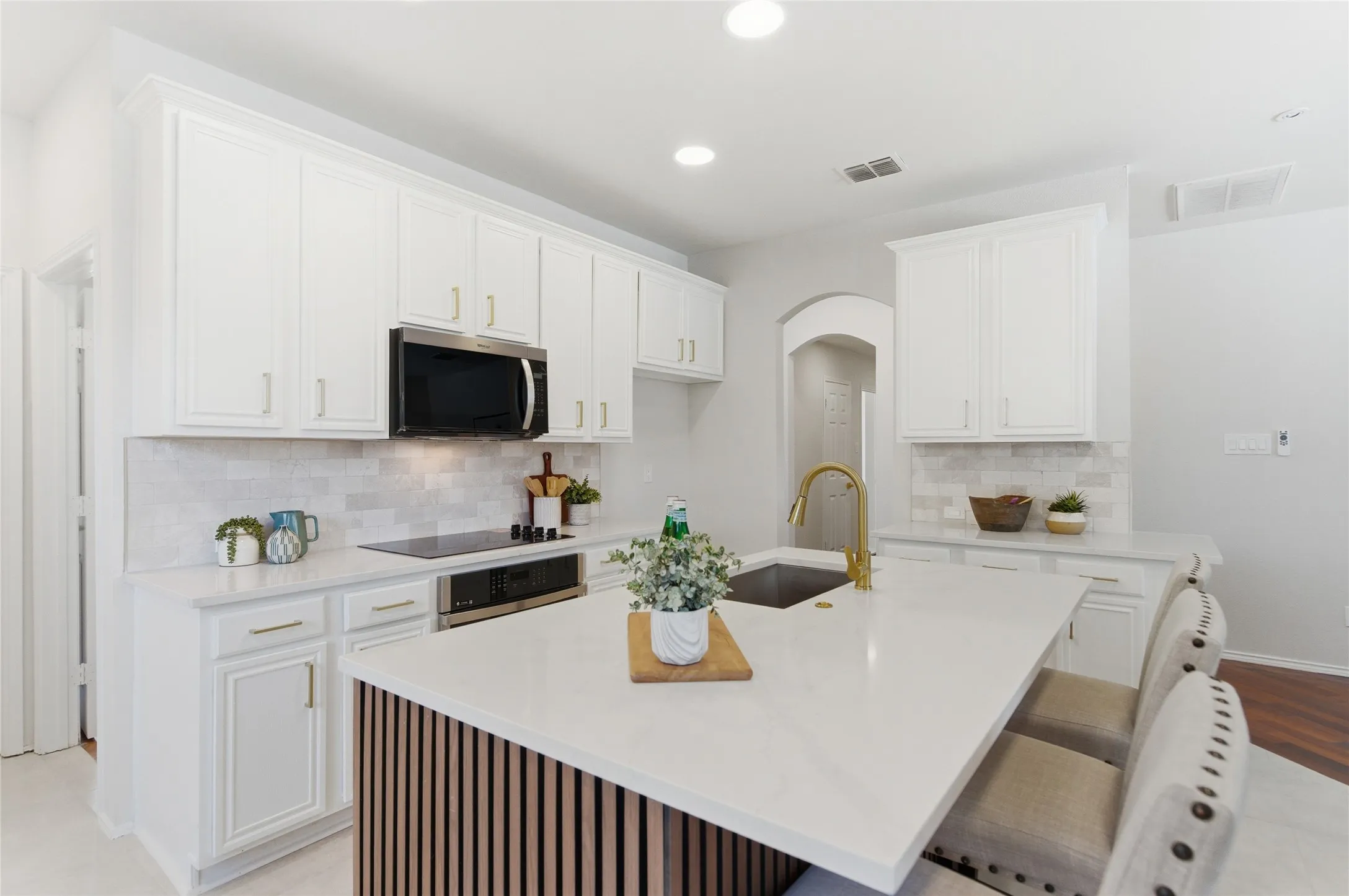 White cabinetry, stainless steel microwave, integrated cooktop, island with solid surface countertop, and undermount sink with gold-finish faucet