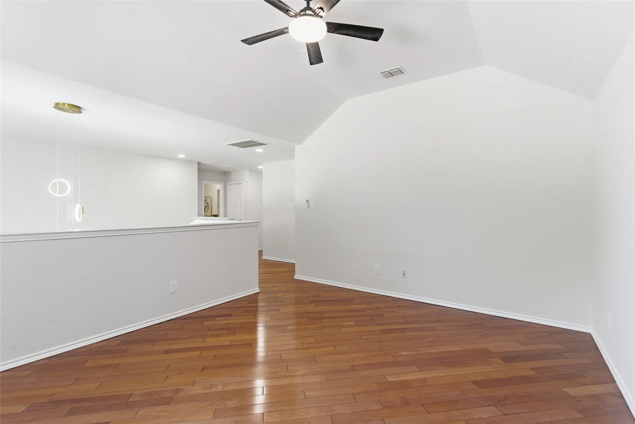 Vaulted ceiling, wood-finish flooring, ceiling fan with light, modern pendant lighting, half-wall partition