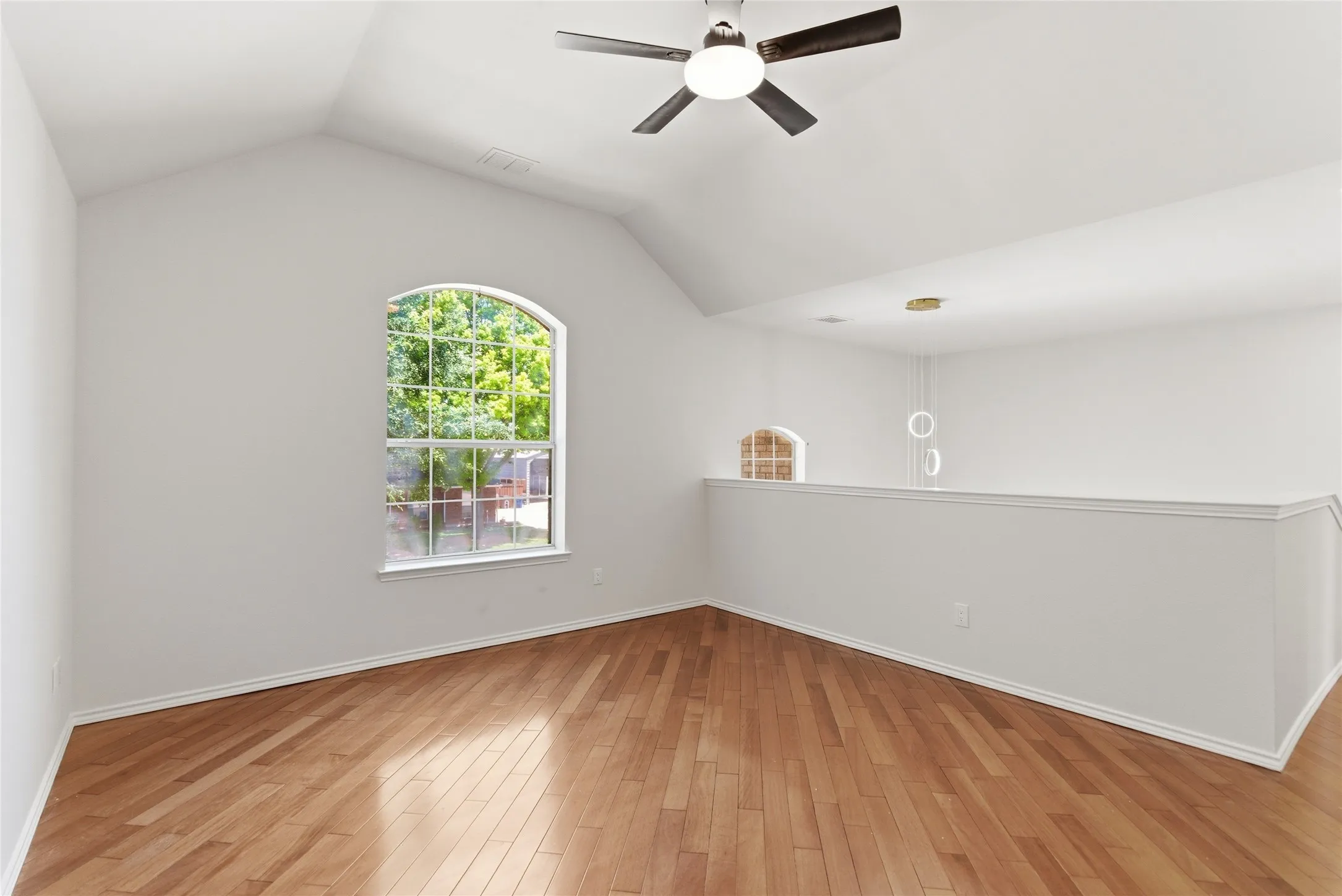 Vaulted ceiling, arched window, wood-finish flooring, ceiling fan, and open railing