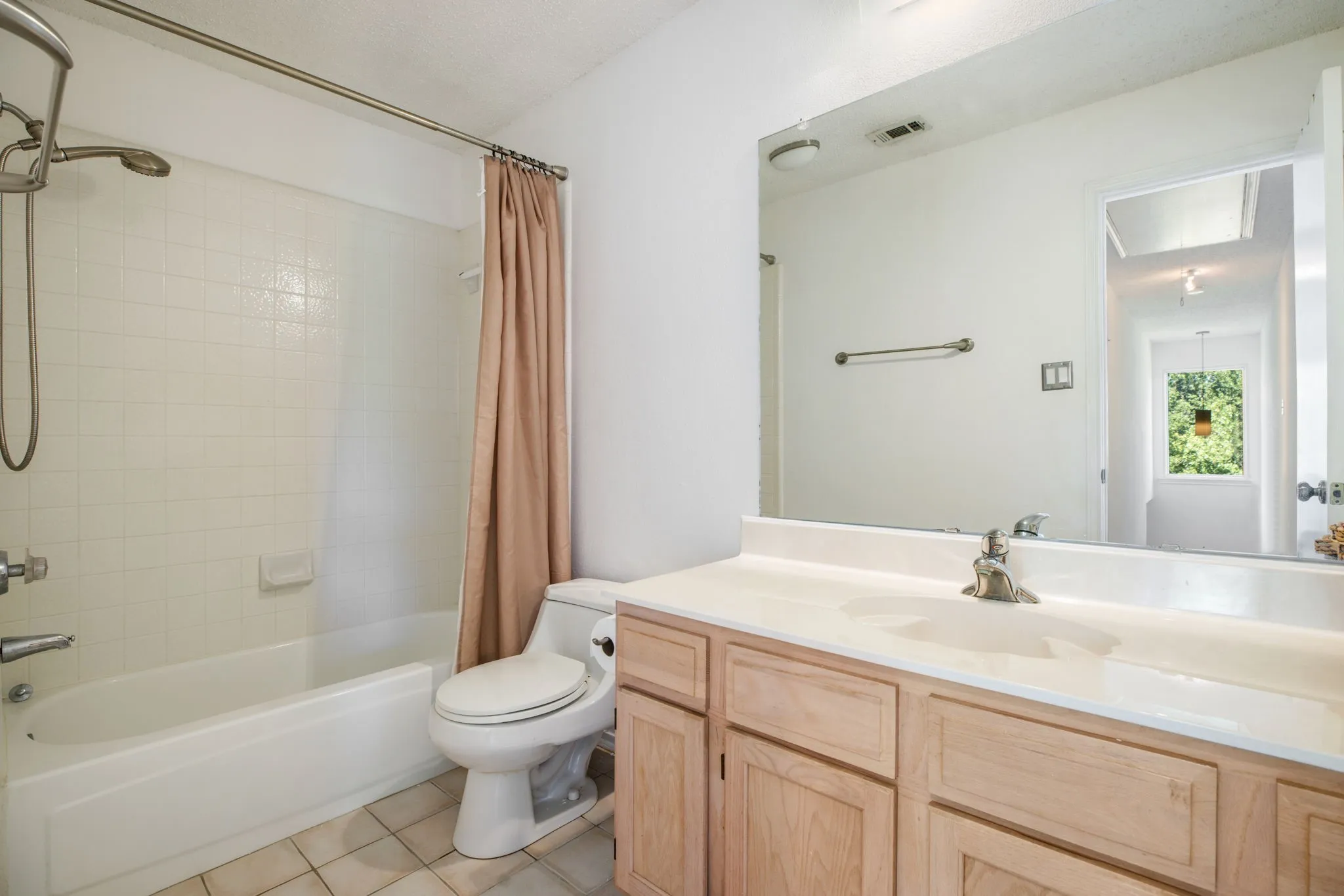 White tile flooring, single vanity with wood-finish cabinetry, integrated sink, and an expansive wall-mounted mirror
