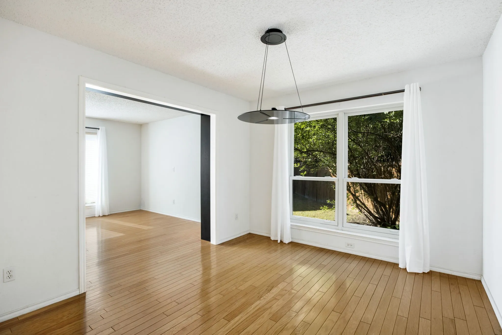 Wood-finish flooring, white walls, modern pendant light fixture, and large window with white casing