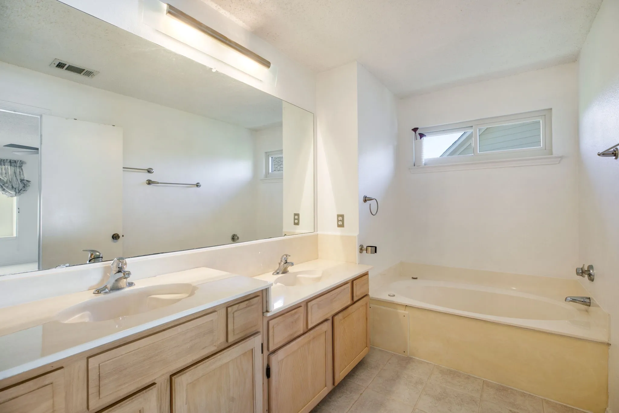 Dual vanity with integrated sinks, light wood-finish cabinetry, and a large wall-mounted mirror