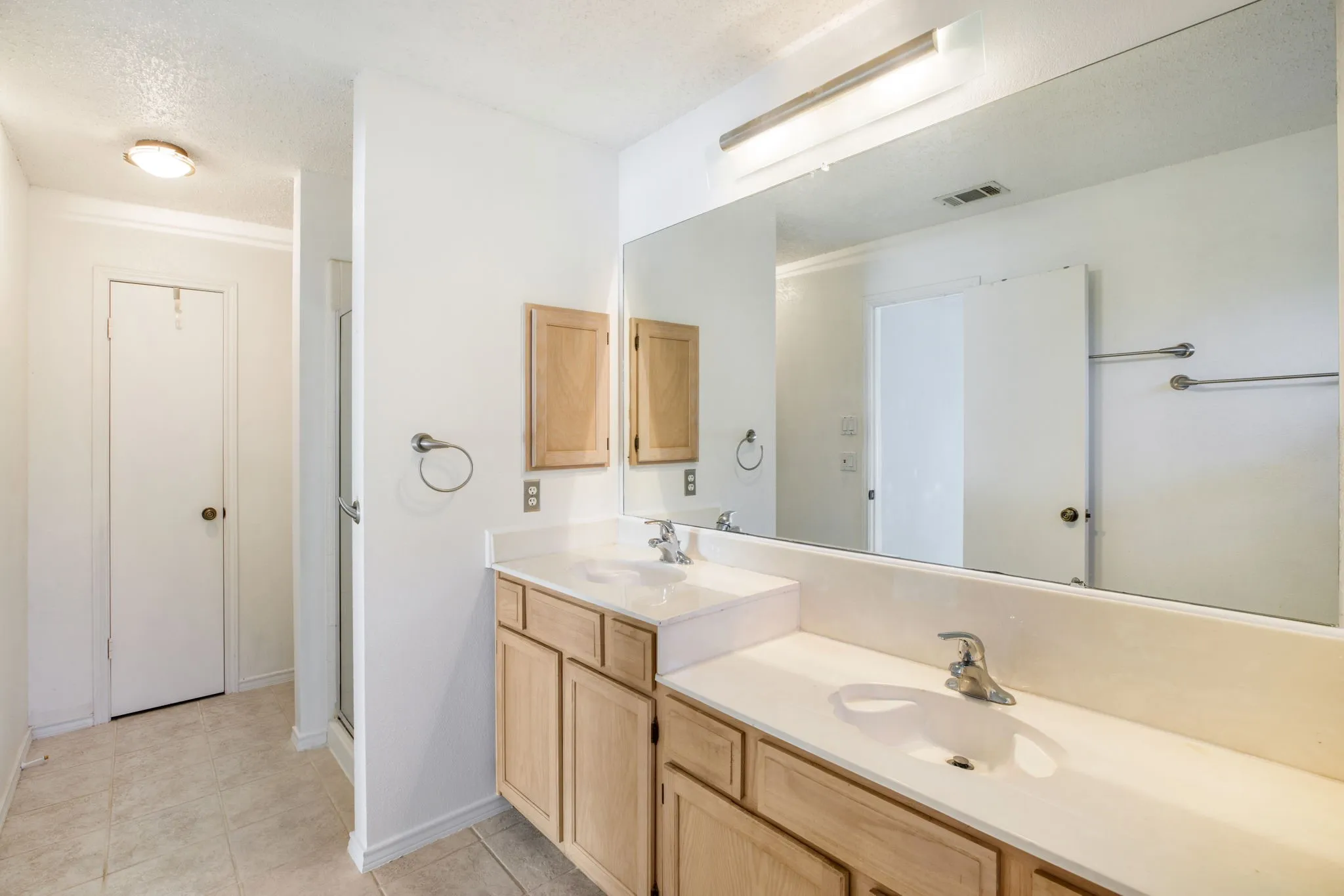 Dual vanity with light wood-finish cabinetry and integrated sinks, complemented by a large wall-mounted mirror