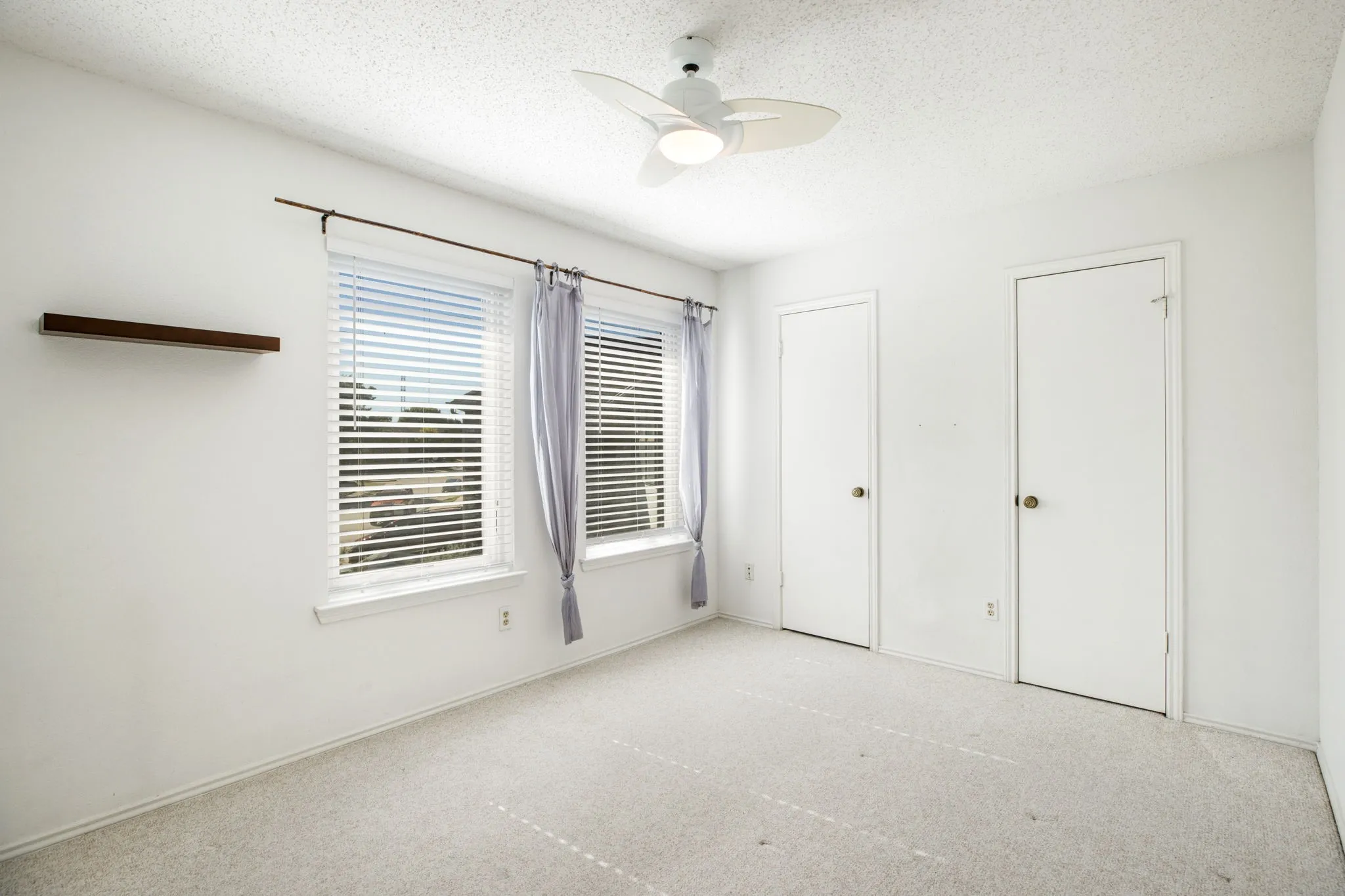 Ceiling fan with integrated lighting, two windows with blinds, built-in floating shelf, and two interior doors