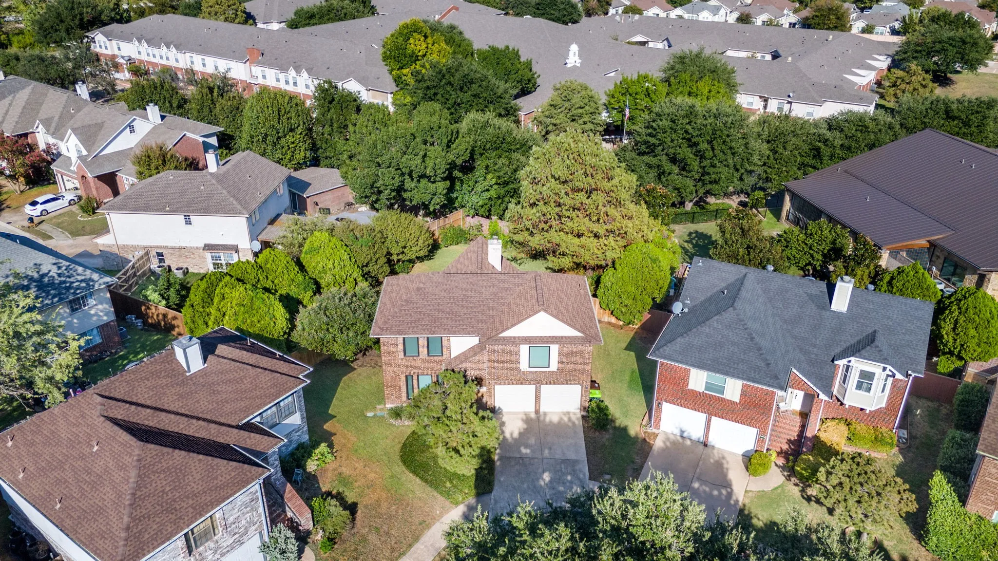 Two-story residence featuring brick siding, a dual-car garage, and mature landscaping