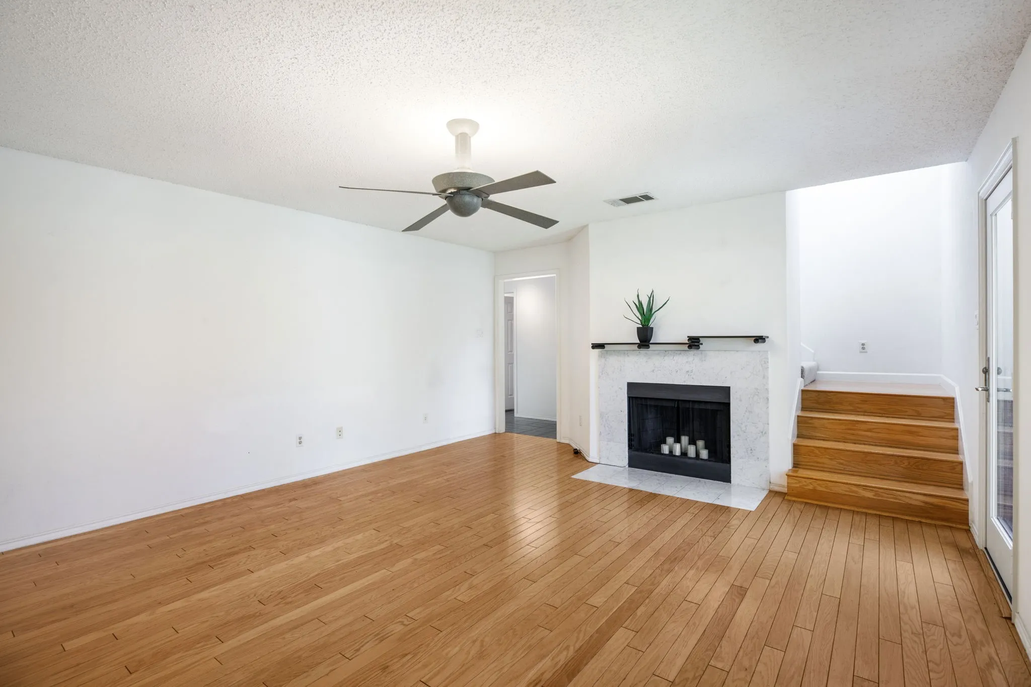 Hardwood flooring, white painted walls, fireplace with stone surround, wood staircase, and ceiling fan