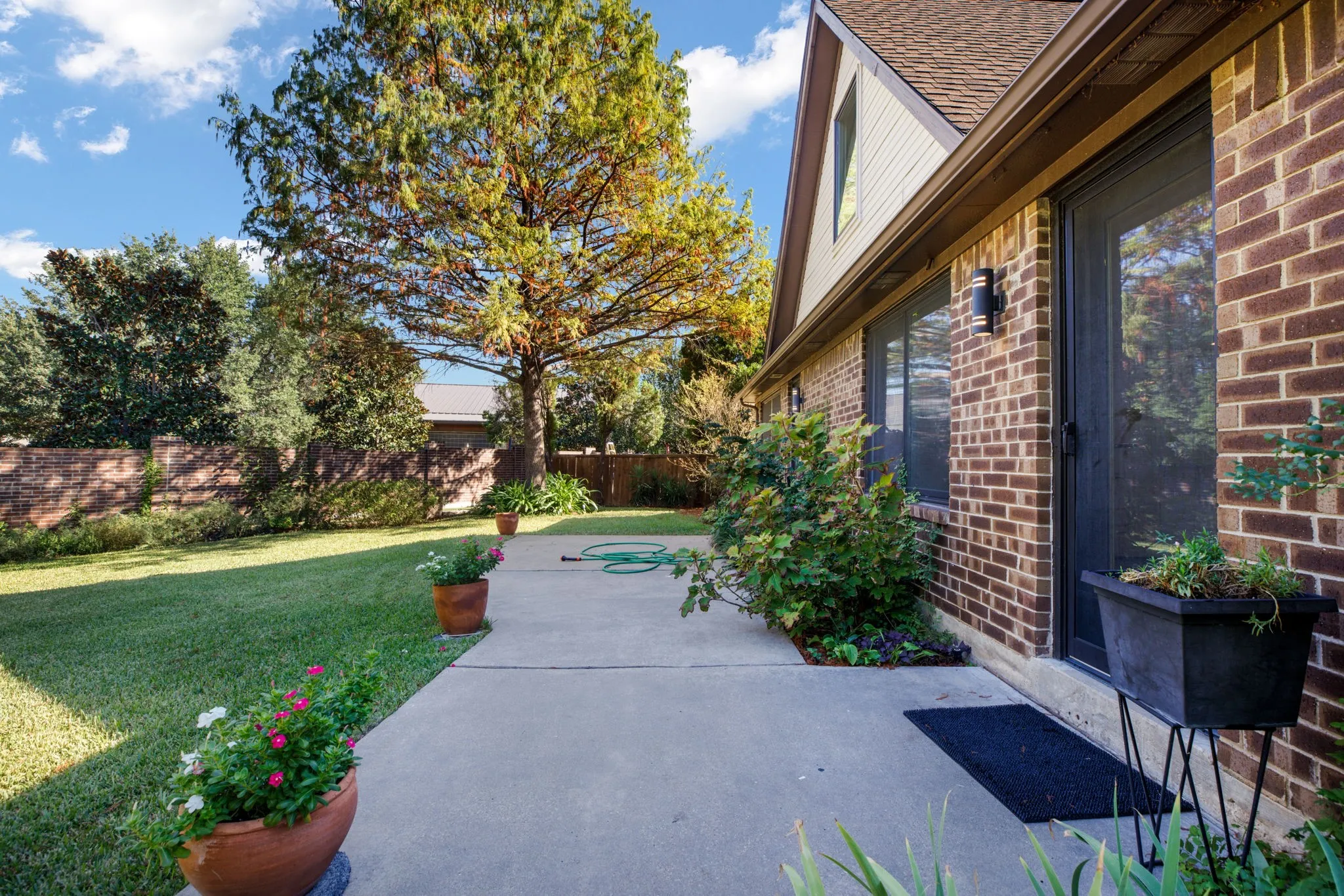 Brick exterior with a gabled roofline, concrete patio, and mature landscaping