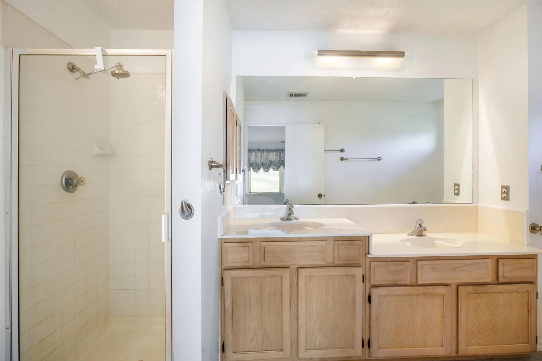 Shower with glass enclosure, dual vanity with integrated sinks, and neutral countertops