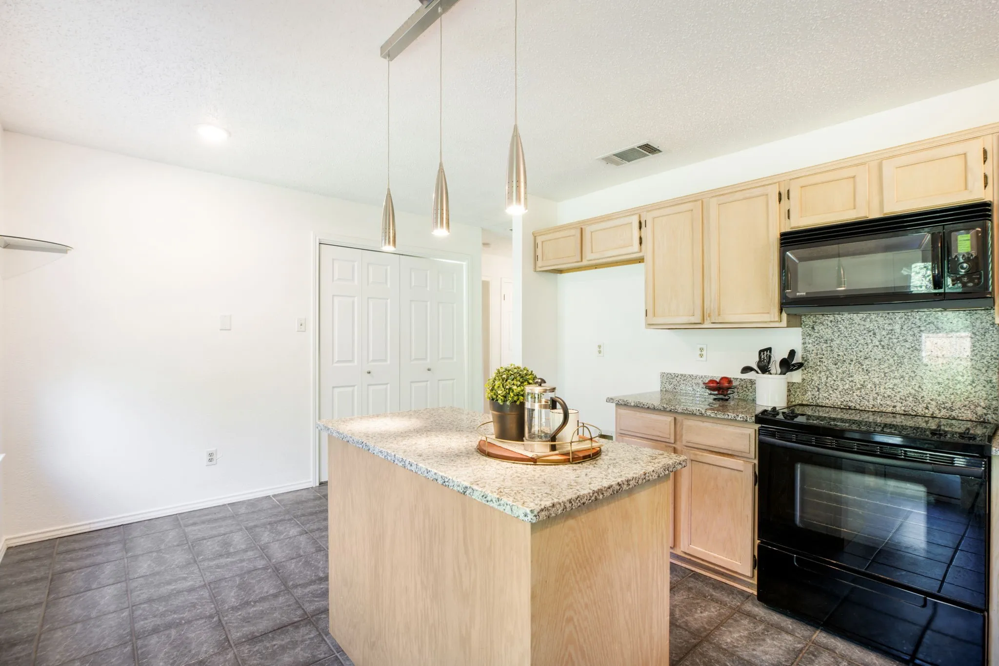 Kitchen featuring a central island with a stone-finish countertop, light wood-finish cabinetry, and dark tile flooring