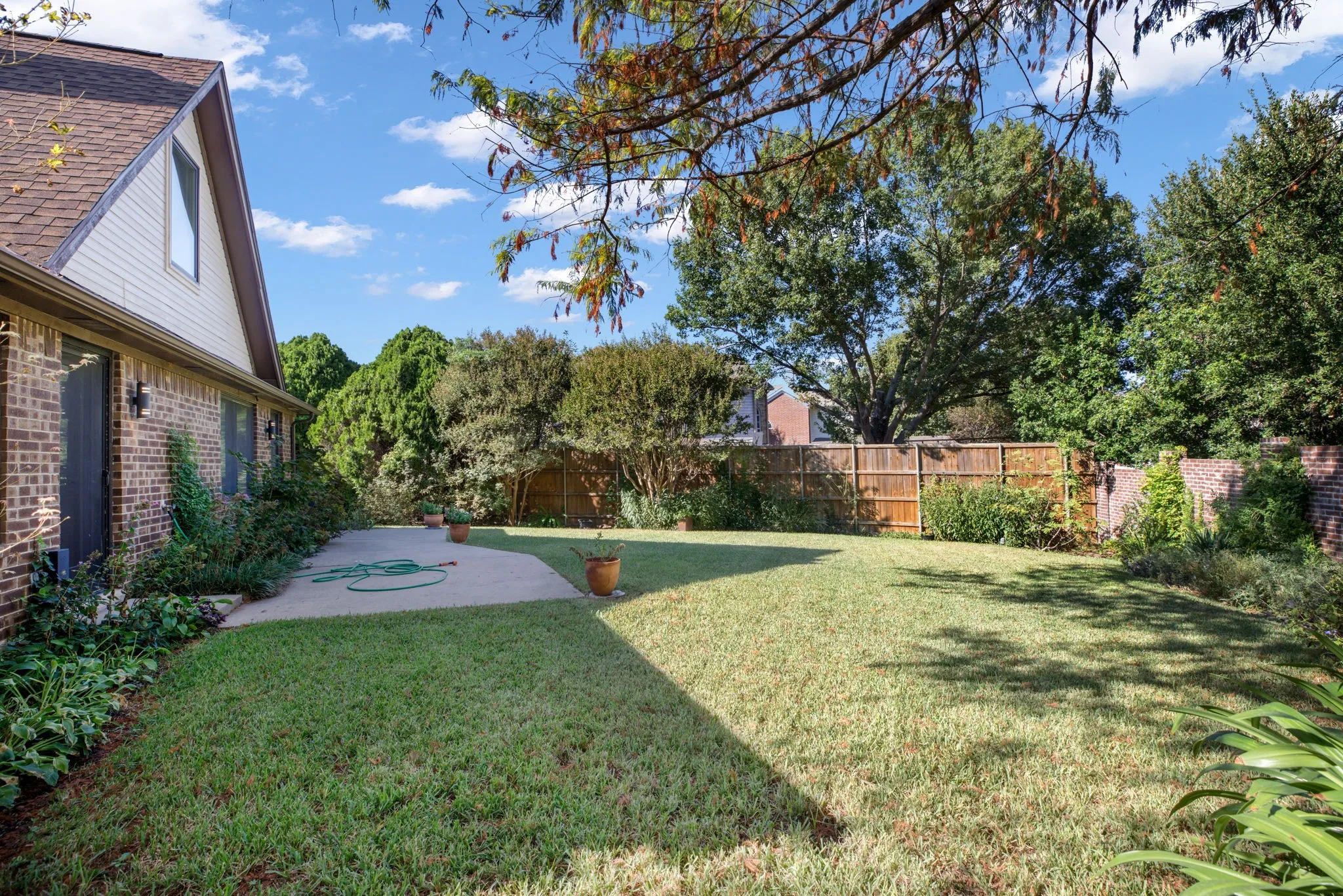 Expansive backyard featuring a manicured lawn, concrete patio, mature trees, and a combination wood and brick privacy fence