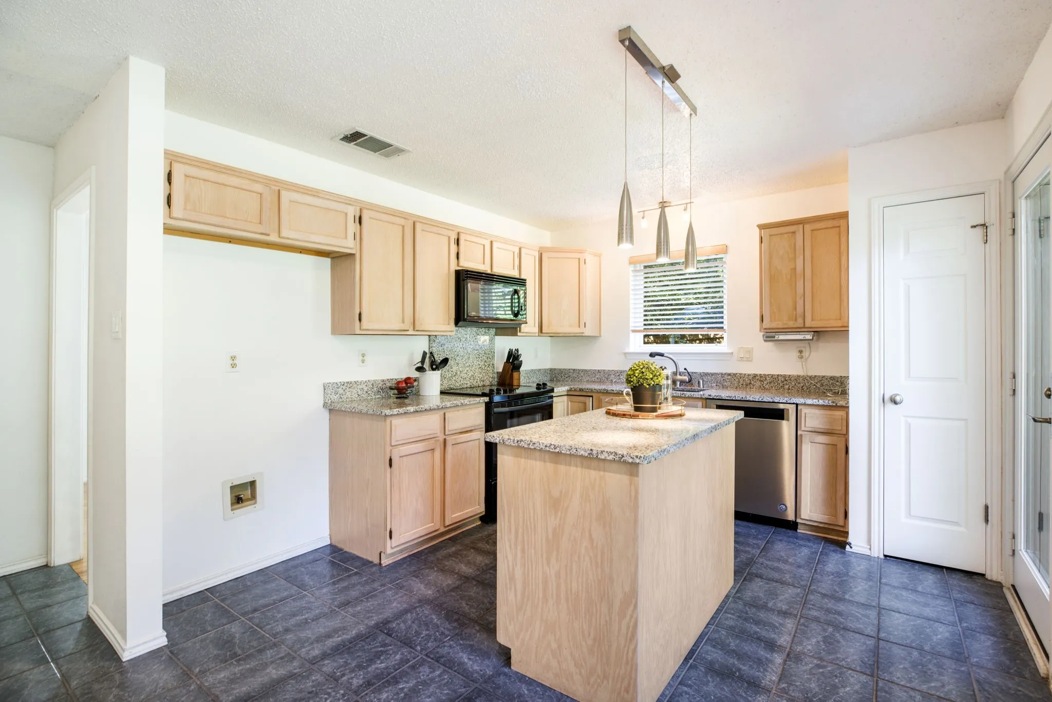 Kitchen featuring an island, light wood-finish cabinetry, granite countertops, tile flooring, and a stainless steel dishwasher