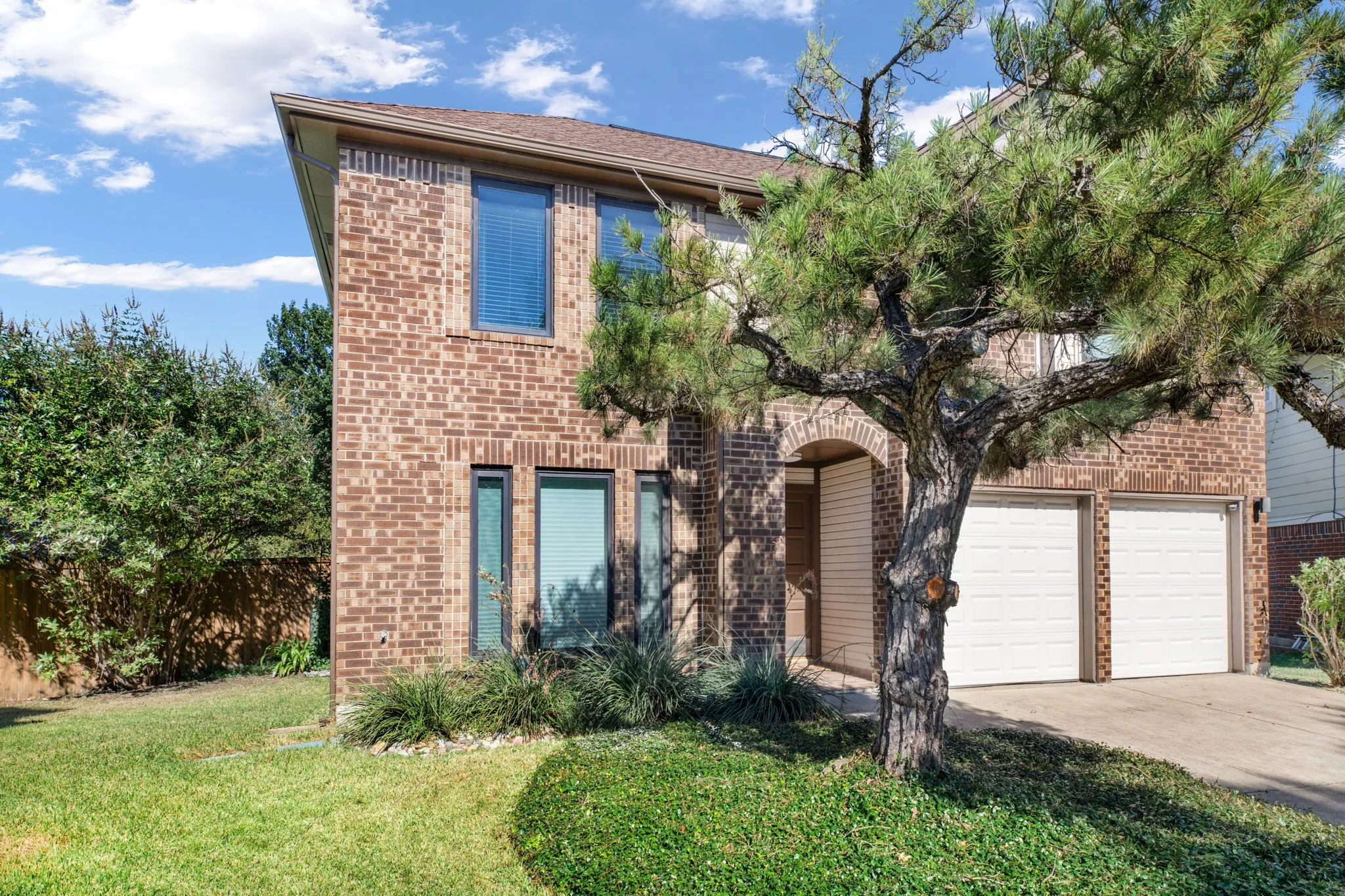 Brick facade with a two-car garage, arched entry, and established landscaping