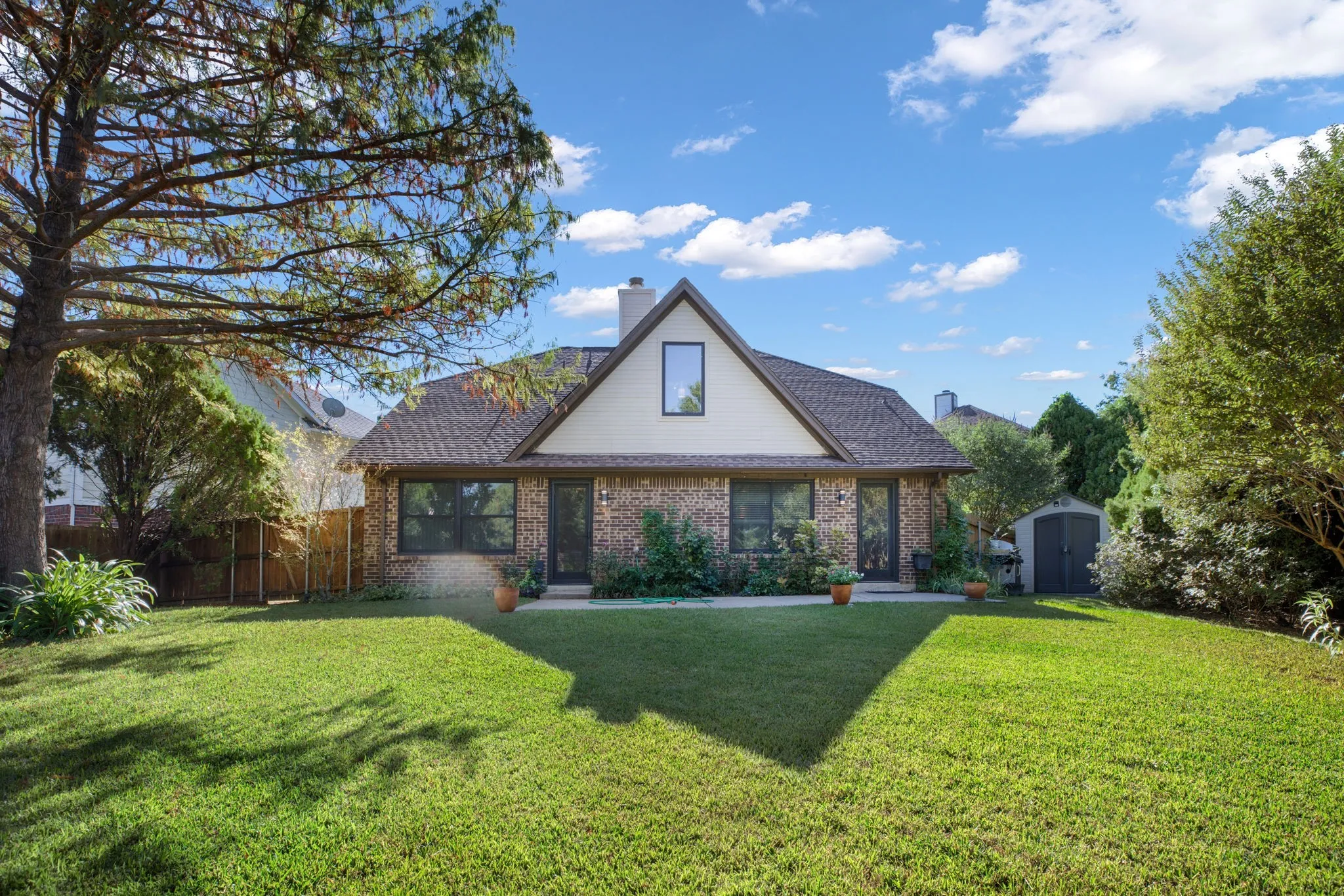 Brick exterior with an A-frame architectural element, featuring a shingled roof, a prominent chimney, and a landscaped yard with mature trees