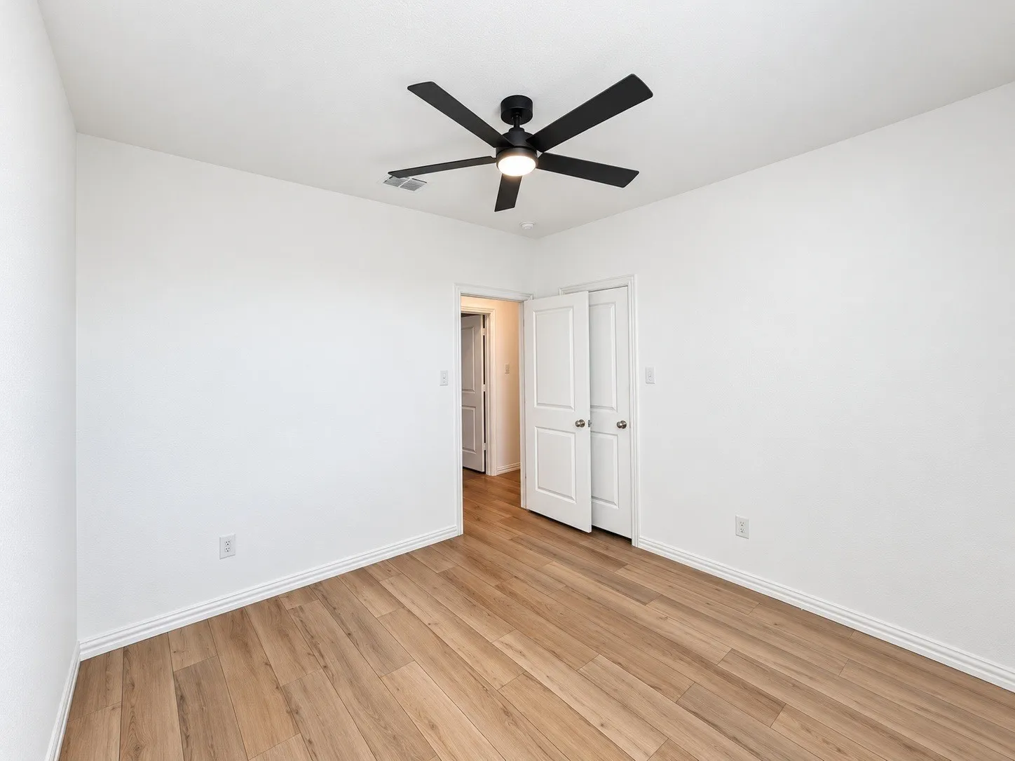 Wood-finish flooring throughout, white painted walls, and a modern black ceiling fan with integrated lighting