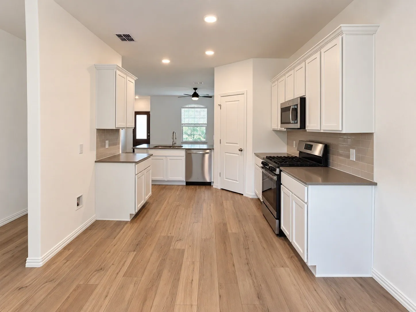 Kitchen featuring wood-finish flooring, recessed lighting, white cabinetry, integrated stainless steel appliances, and a subway tile backsplash