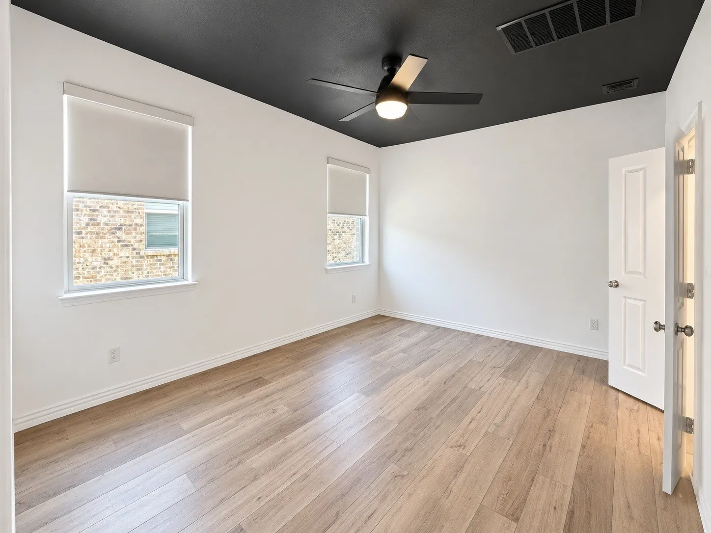 Wood-finish flooring, white walls, and a contrasting black ceiling with a ceiling fan