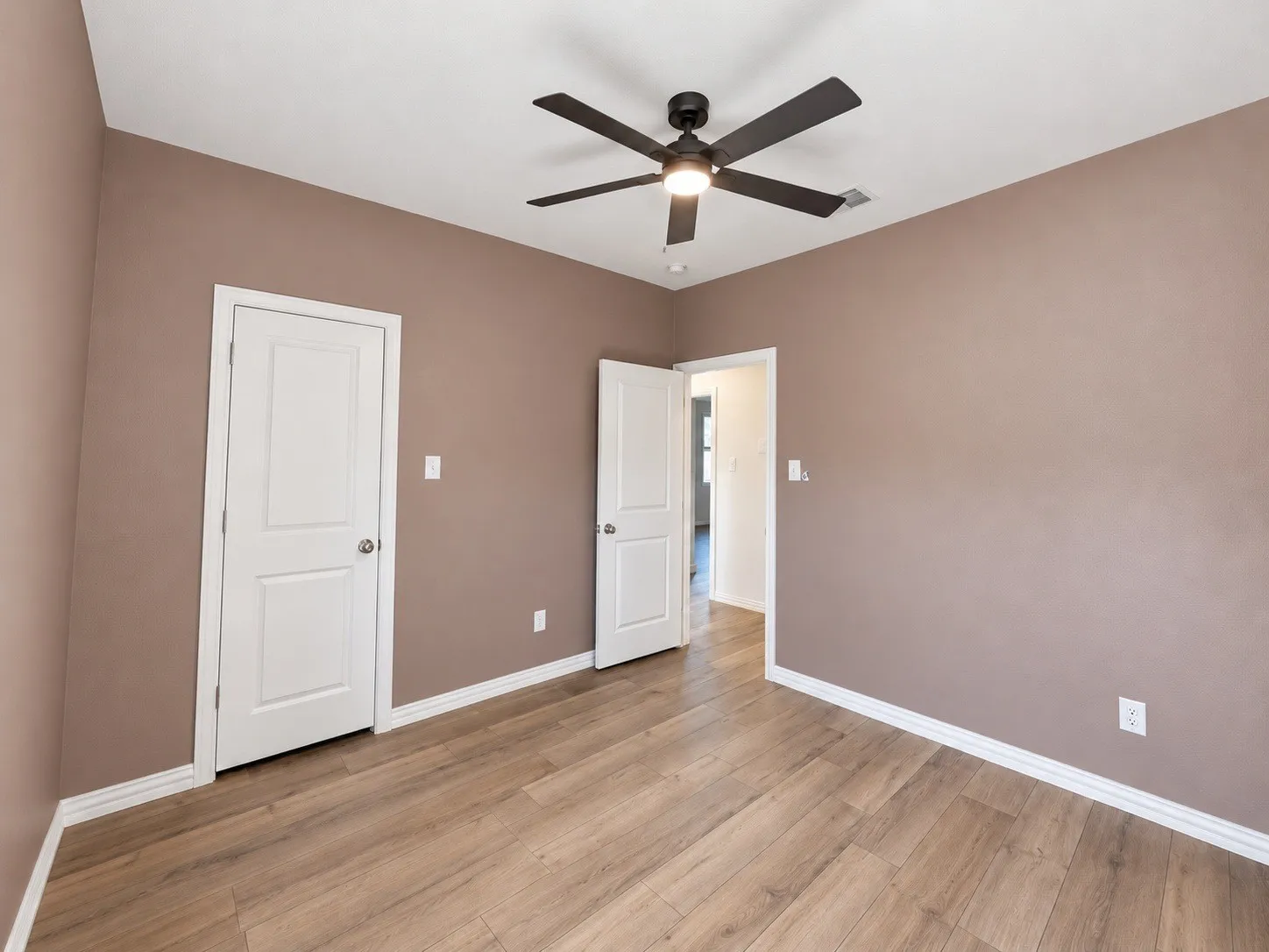 Wood-finish flooring, ceiling fan, white trim, and solid core doors