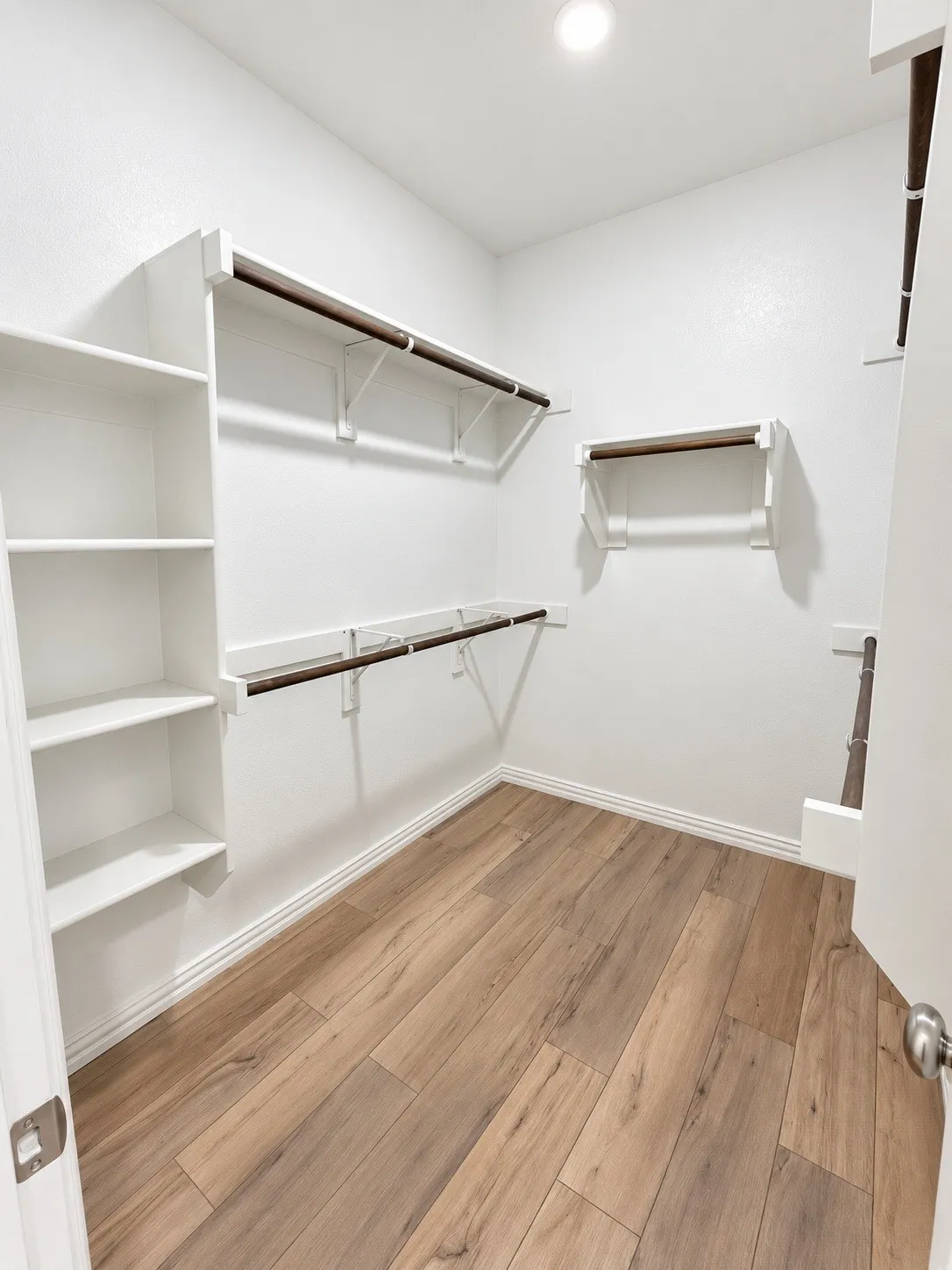 White interior walls, wood-finish flooring, recessed ceiling lighting, built-in shelving, and multiple hanging rods