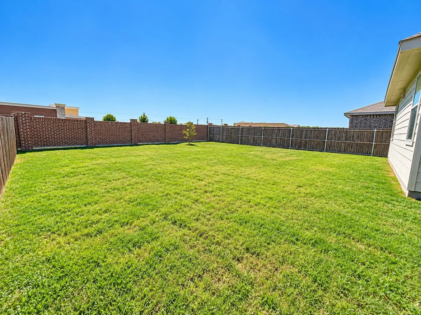 Expansive backyard featuring a large grass lawn, wood privacy fencing, and a brick privacy fence with stone accents