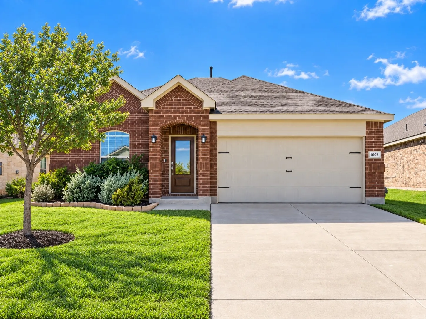Brick exterior with an arched entry, mature landscaping, and an attached two-car garage