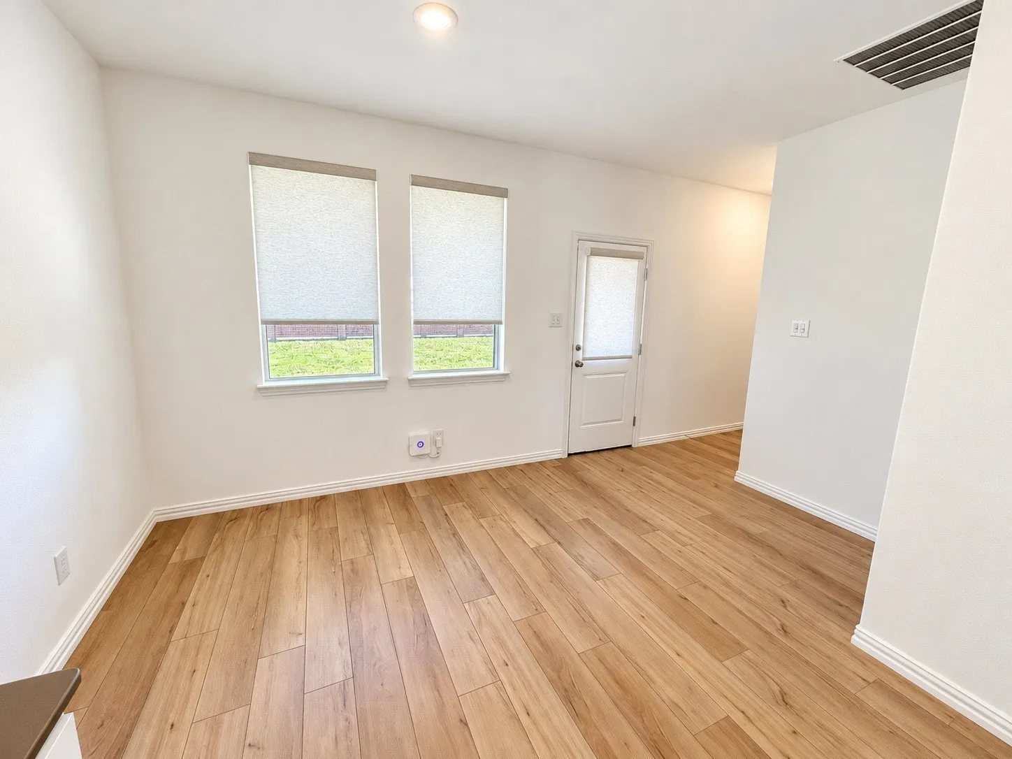 Light wood-finish flooring, recessed ceiling lighting, and white walls- virtually staged.
