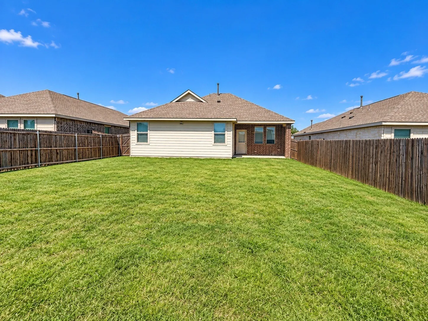 Expansive grassy yard with wood fencing, brick and siding exterior, and a rear entry door