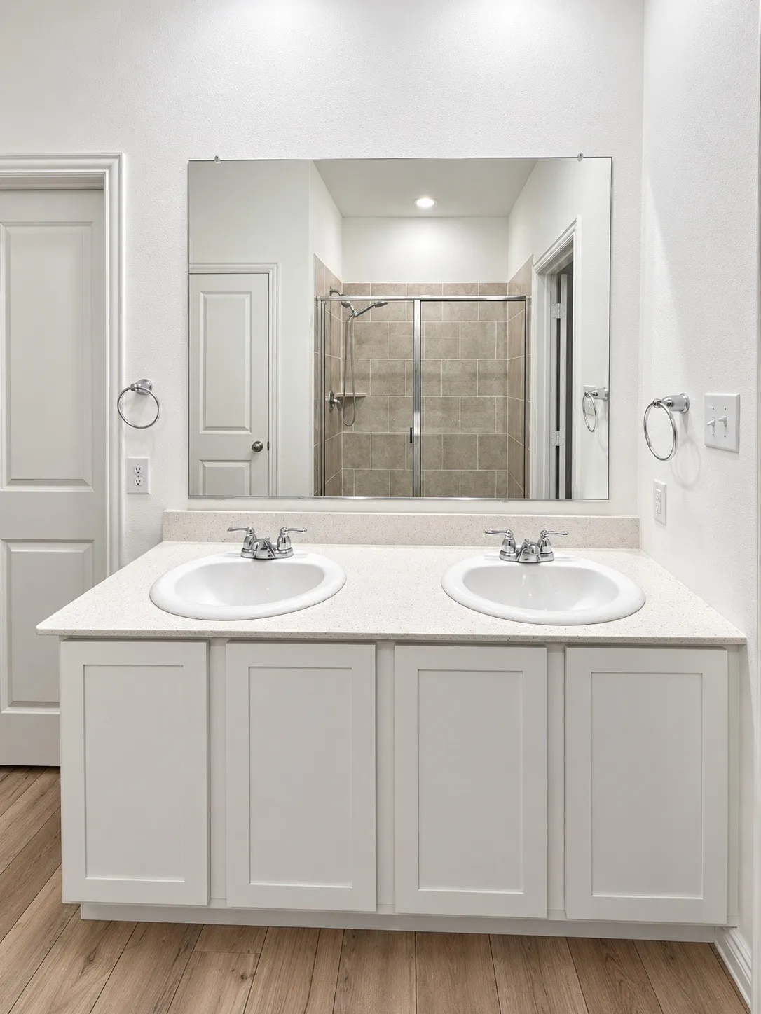 Dual undermount sinks with chrome faucets, white shaker-style vanity cabinetry, light-toned countertop, and a large wall-mounted mirror