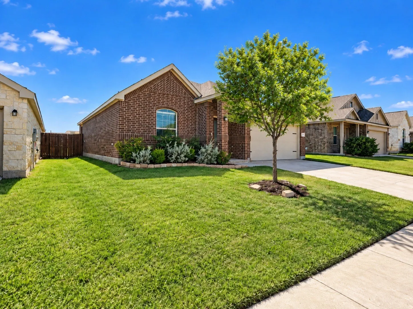Brick exterior, arched window, attached garage, concrete driveway, mature landscaping