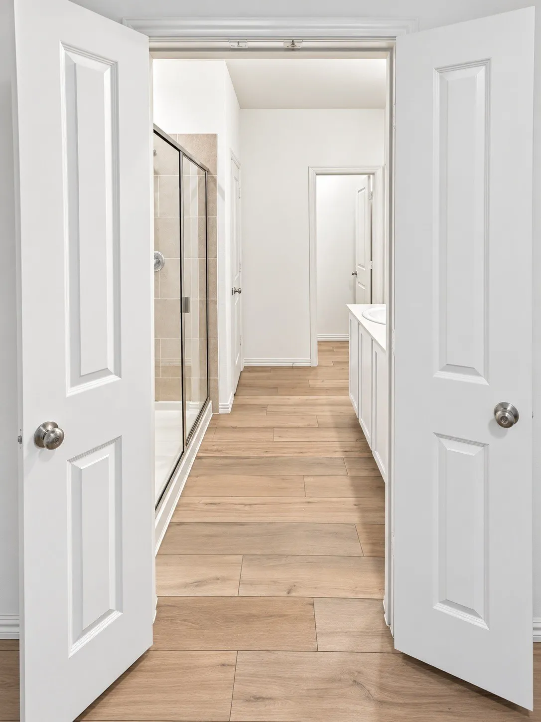 Wood-finish flooring throughout, bright white walls, and a glass-enclosed shower