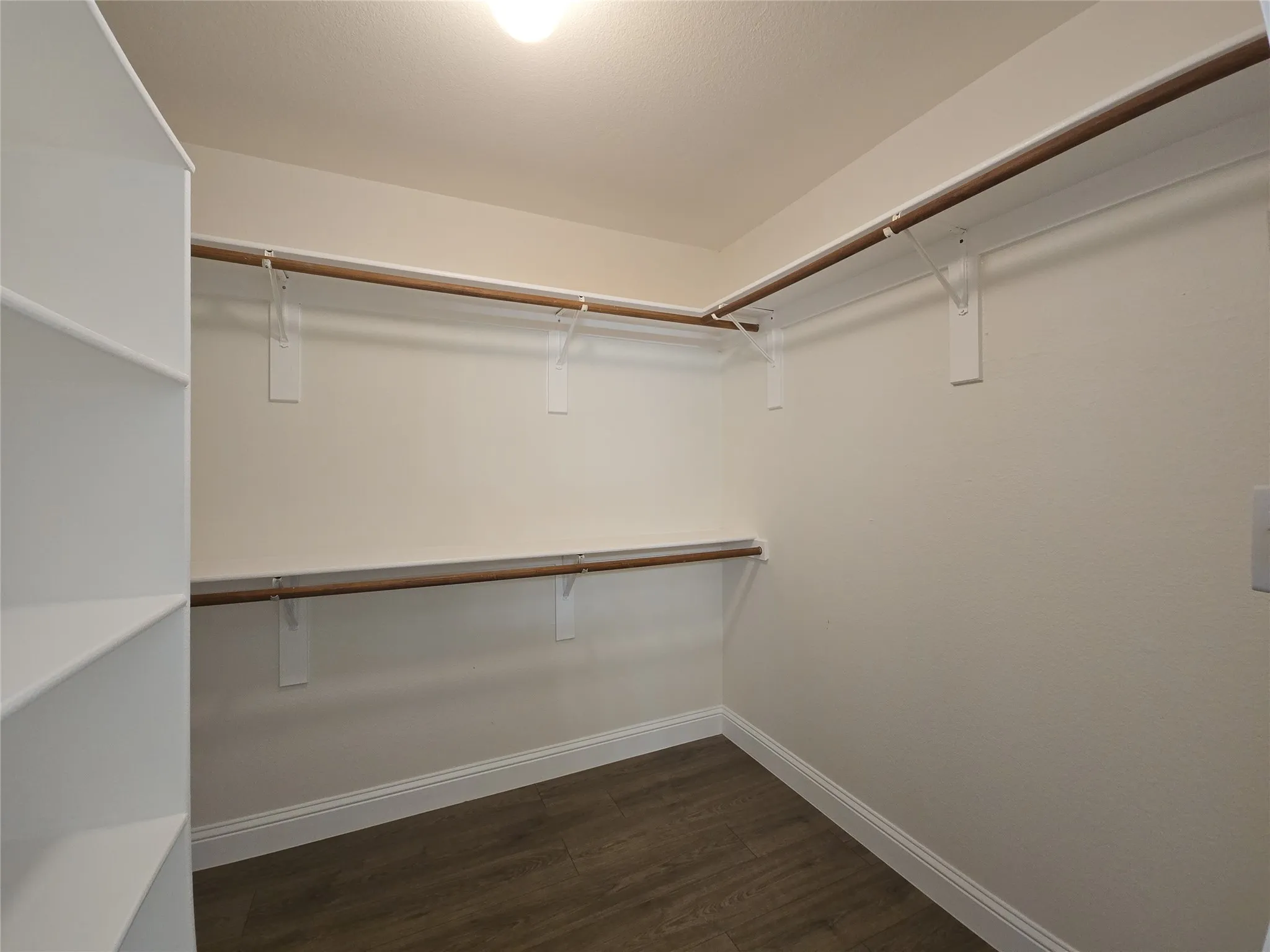 Walk-in closet featuring wood-finish flooring, built-in shelving, and dual clothes rods